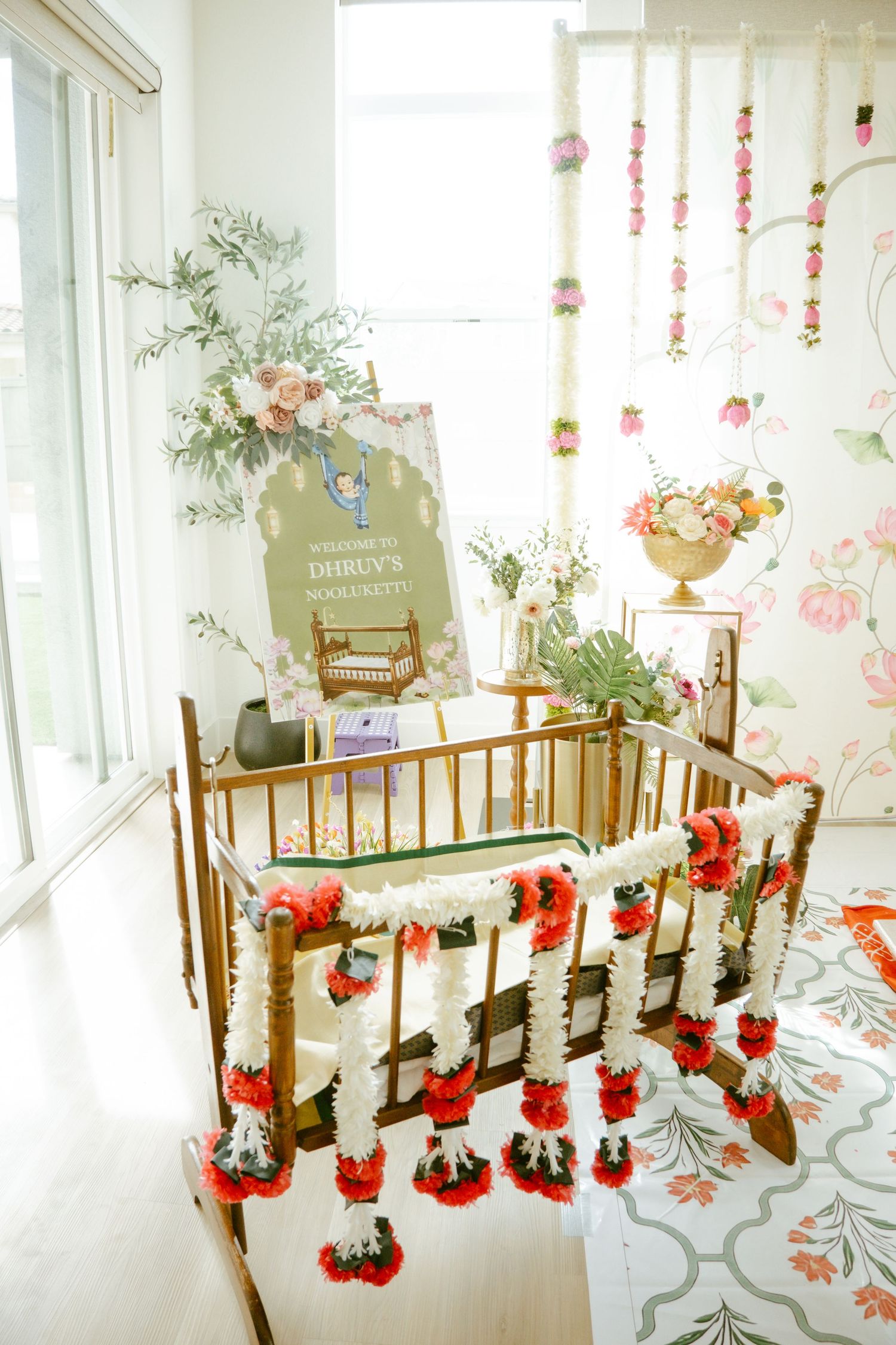 Gold crib adorned with red and white floral garlands at an elegant baby shower with welcome sign.