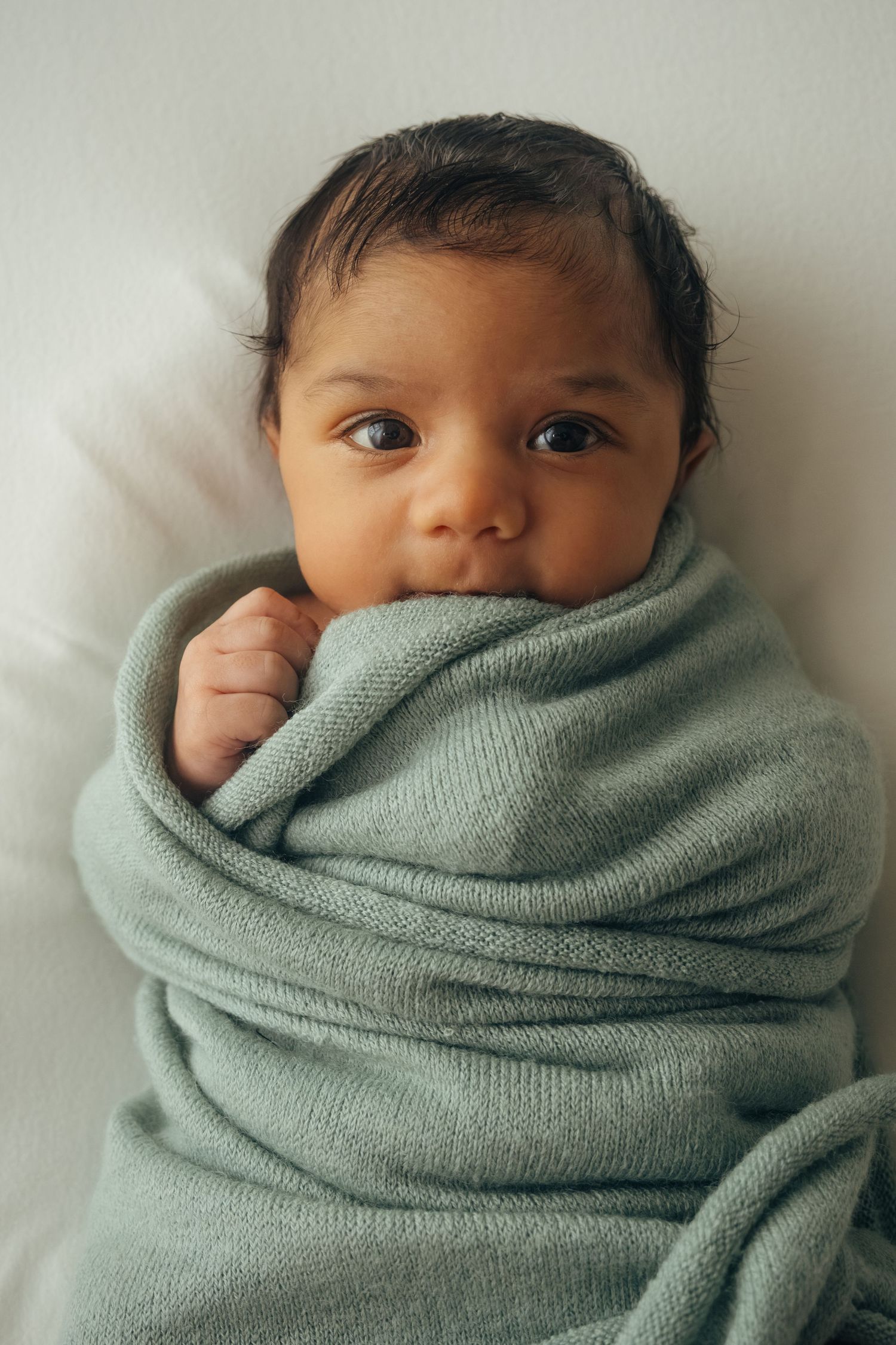 Baby wrapped in a soft mint green blanket looking at camera.