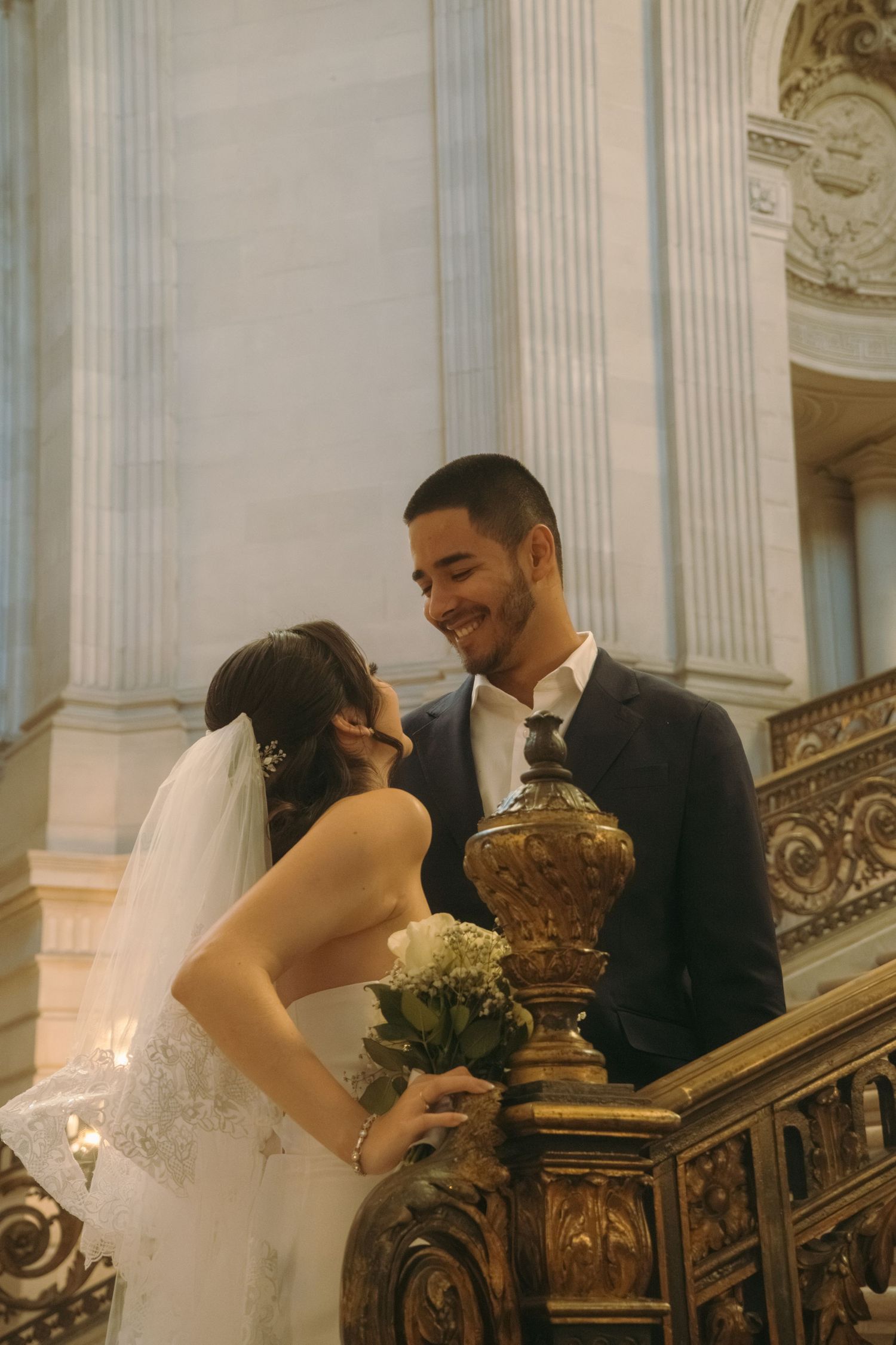 A romantic moment captured on an ornate marble staircase with elegant columns and architectural details.