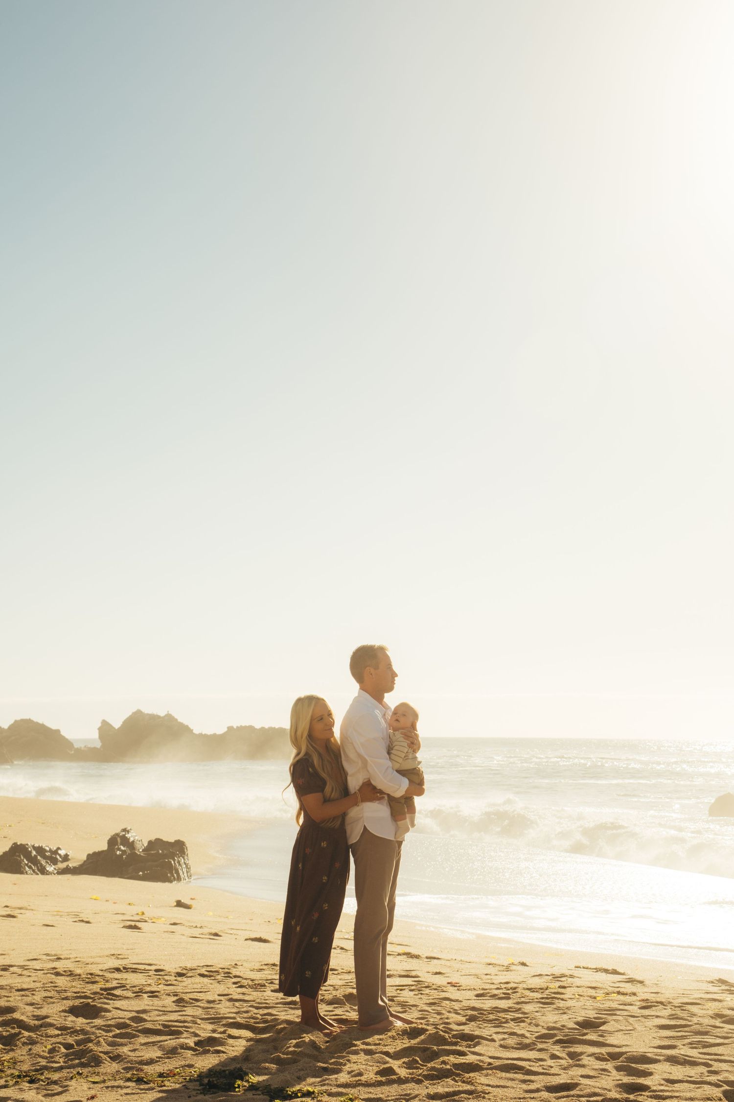 Silhouettes of a family standing together on a beach at sunset with waves crashing behind them.