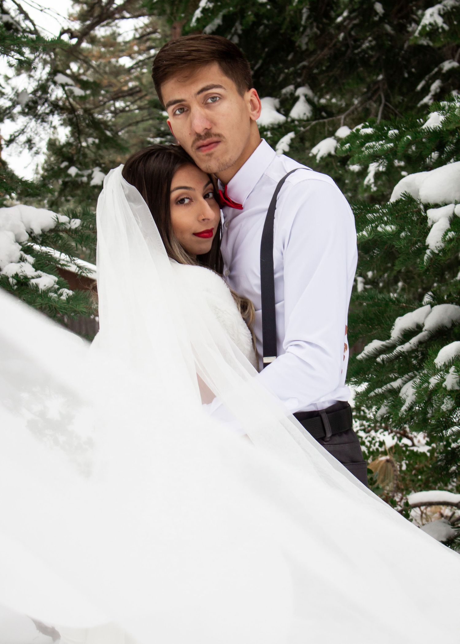 Playful winter wedding portrait with bride's dress flowing in snowy forest setting.
