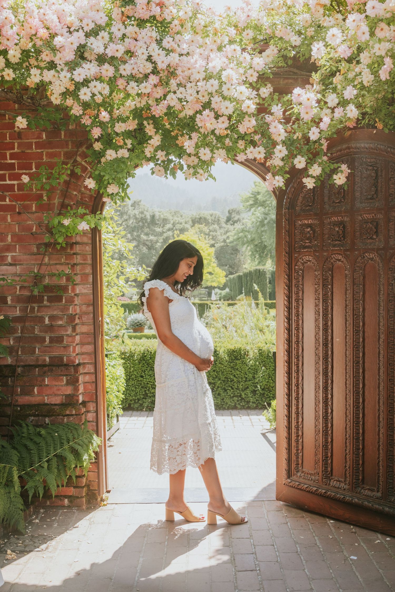 White dress silhouettes under blooming cherry blossoms and brick archway.