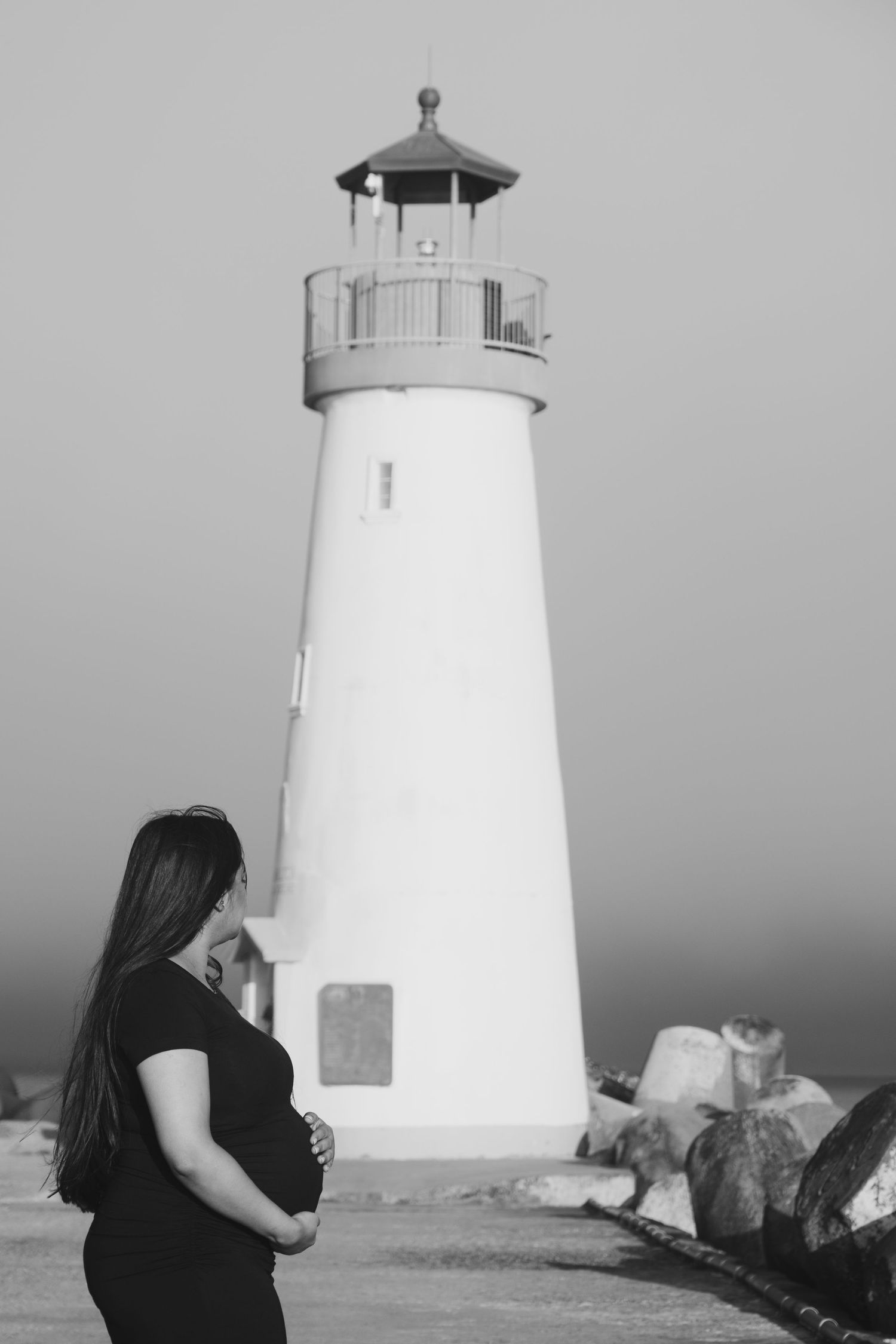 A white lighthouse stands tall against an overcast sky in black and white.