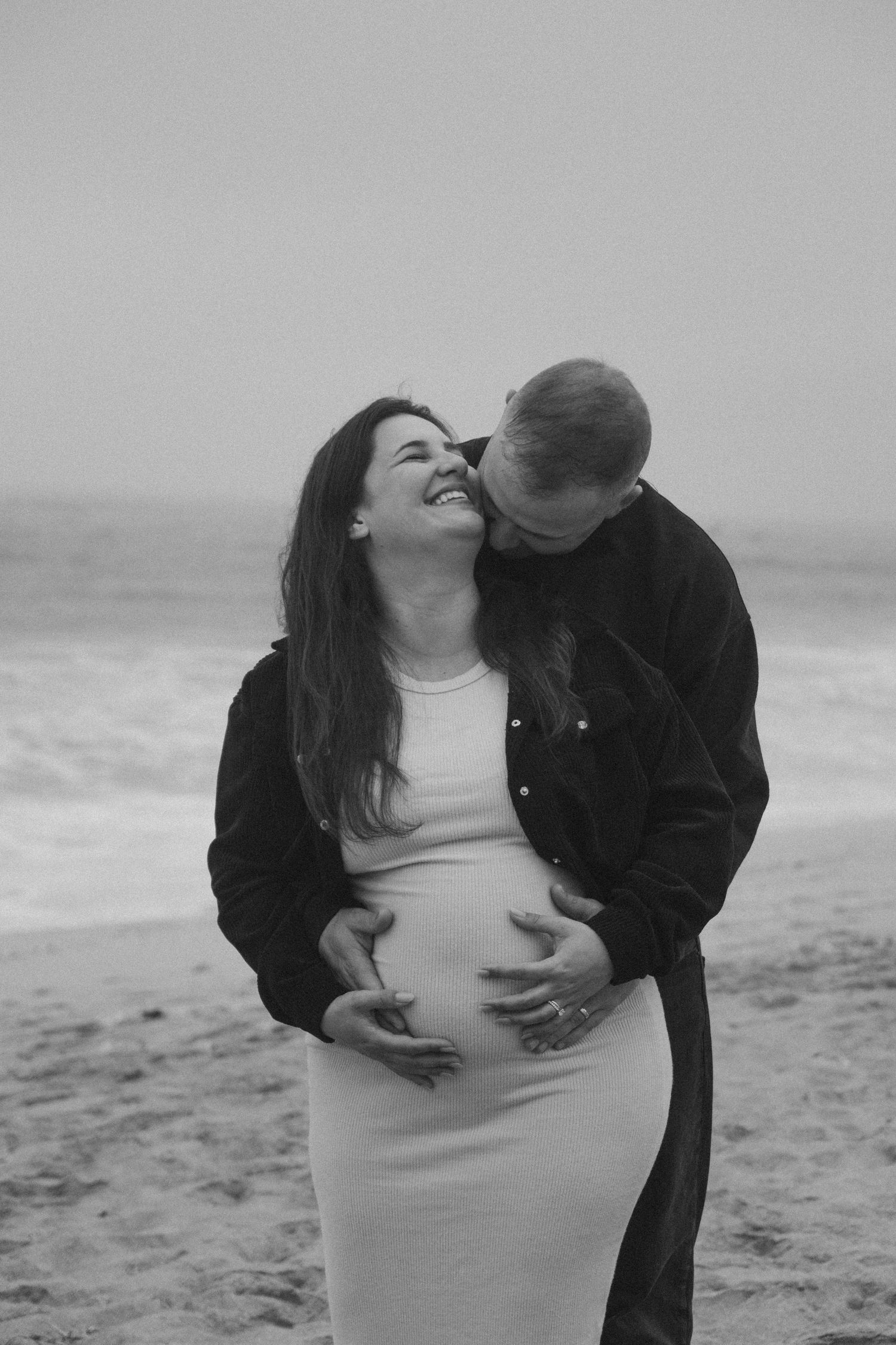 Intimate black and white maternity photos captured on windswept beach.