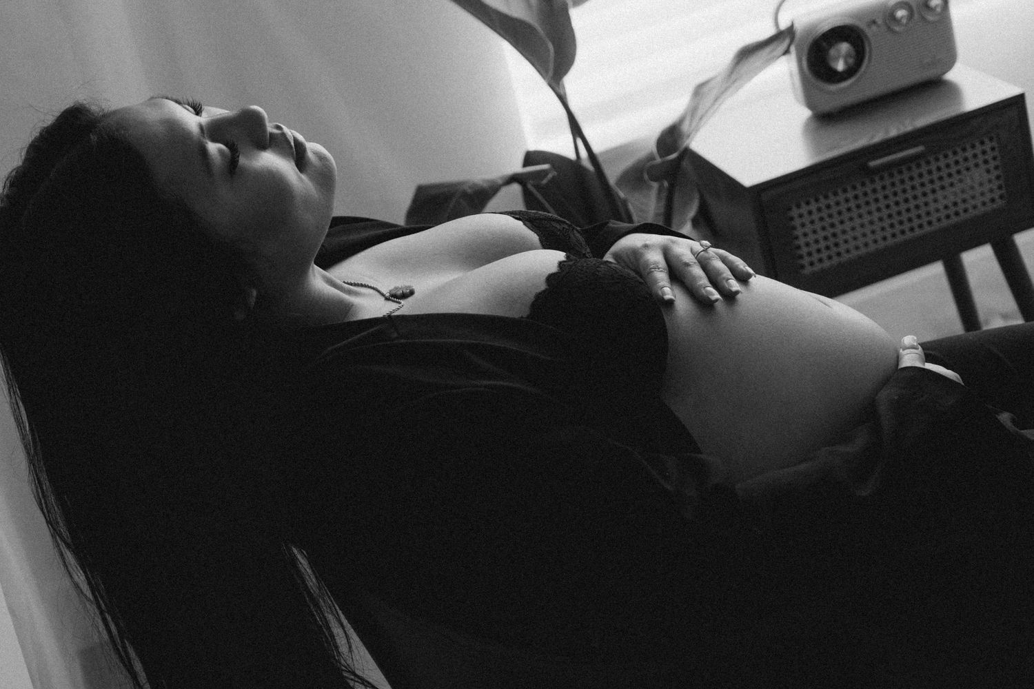 A black and white photograph shows someone reclining on a bed with a camera visible in the background.