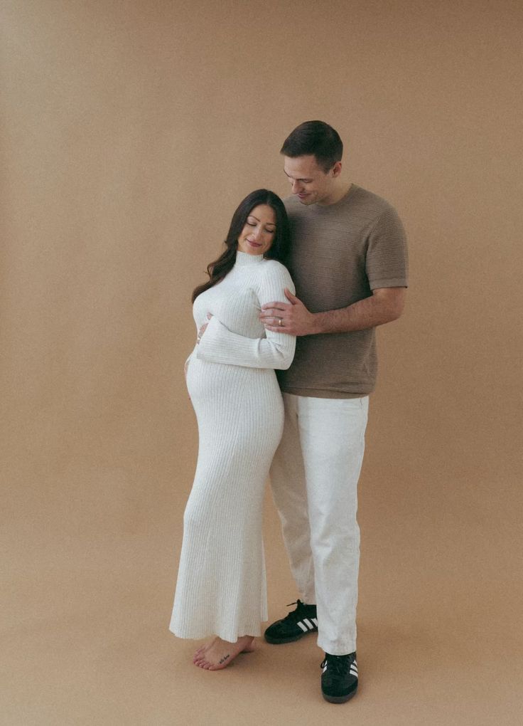 Artistic maternity portraits with couple in white and cream tones against neutral backdrop.