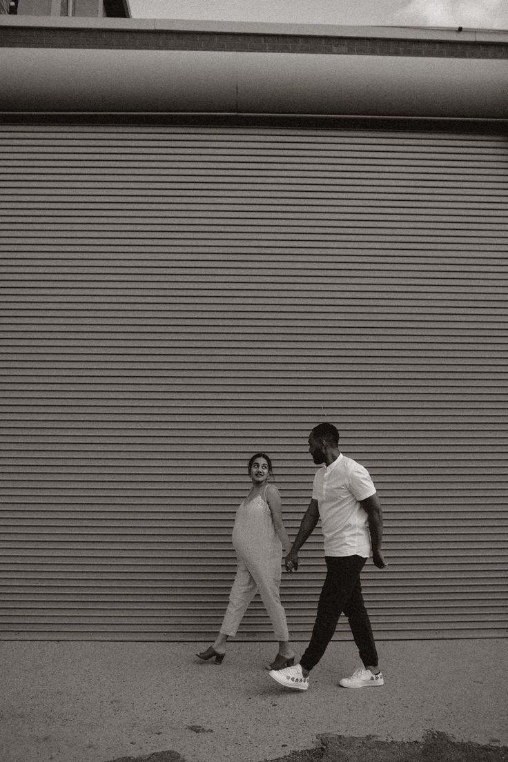 Black and white artistic couple poses against industrial metal garage door.