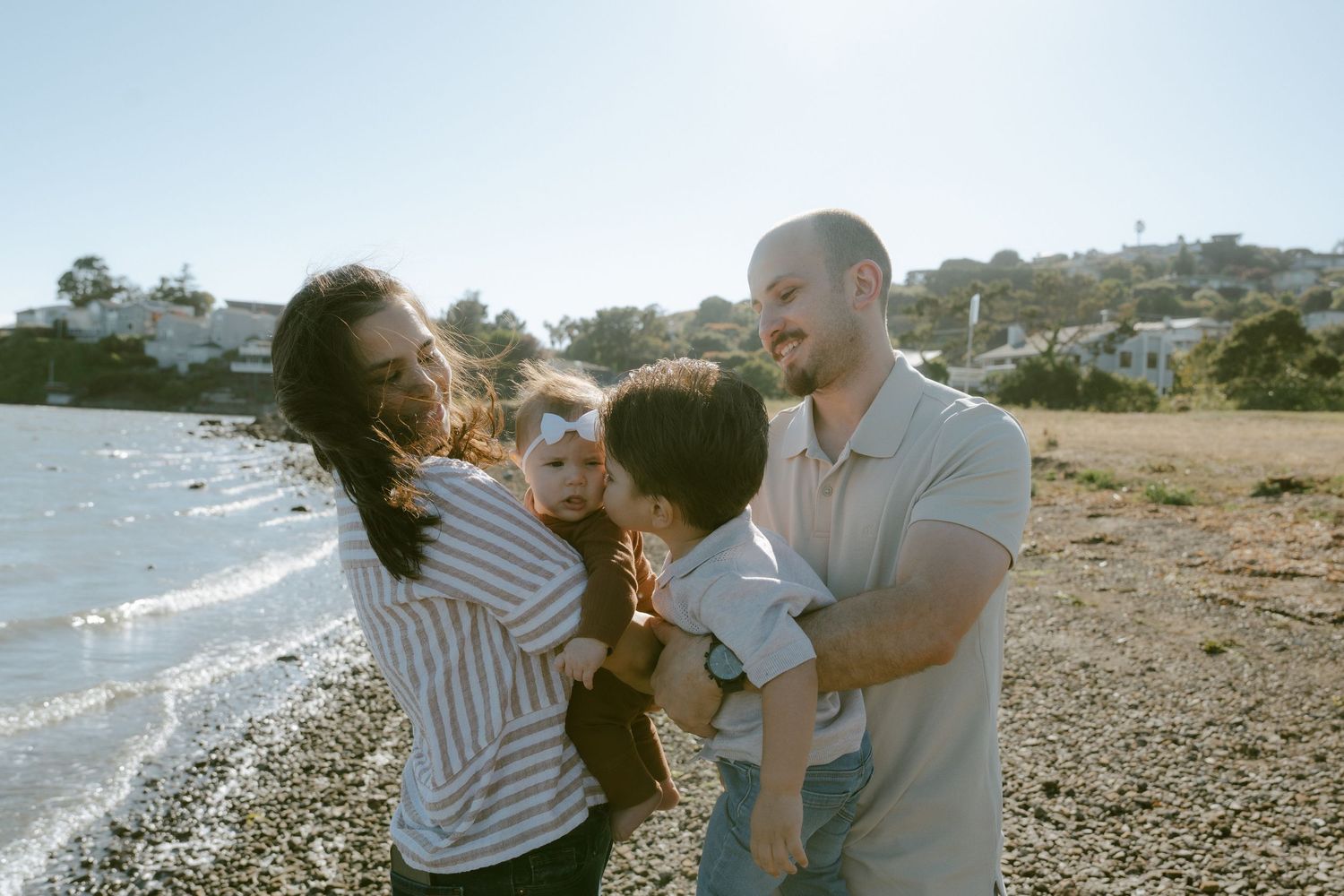 Happy family with two young children enjoying a sunny day on a rocky beach near a coastal town.