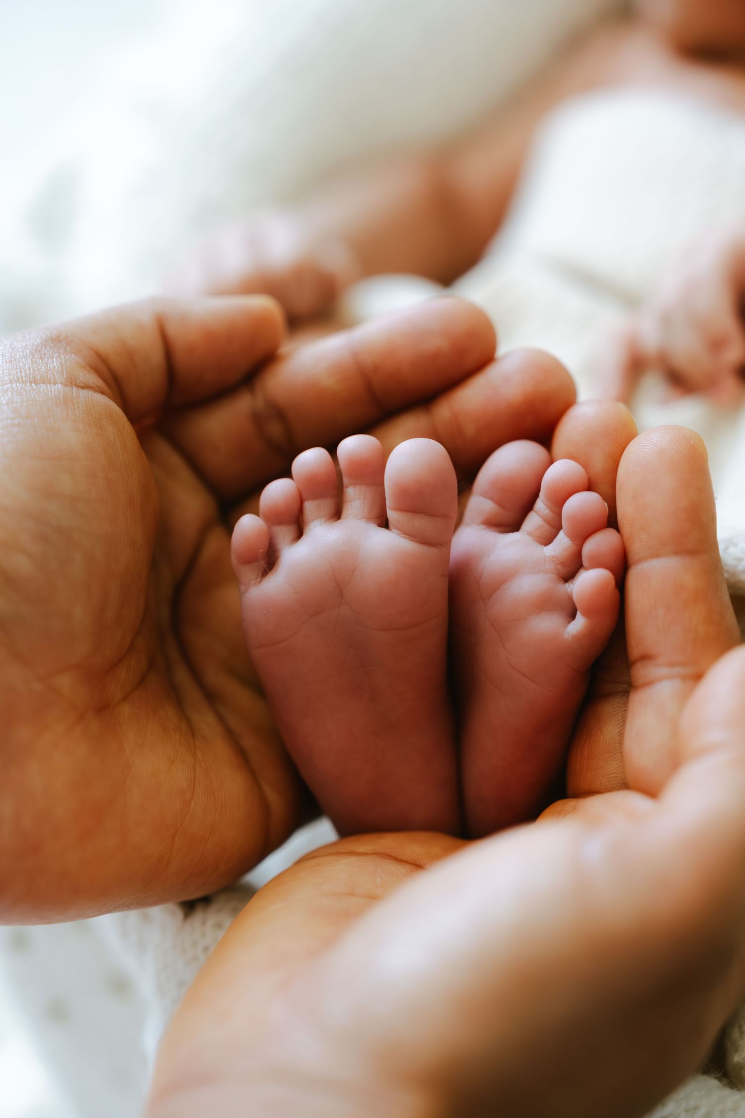 Adult hands gently cradling the tiny feet of a newborn baby on a white blanket.