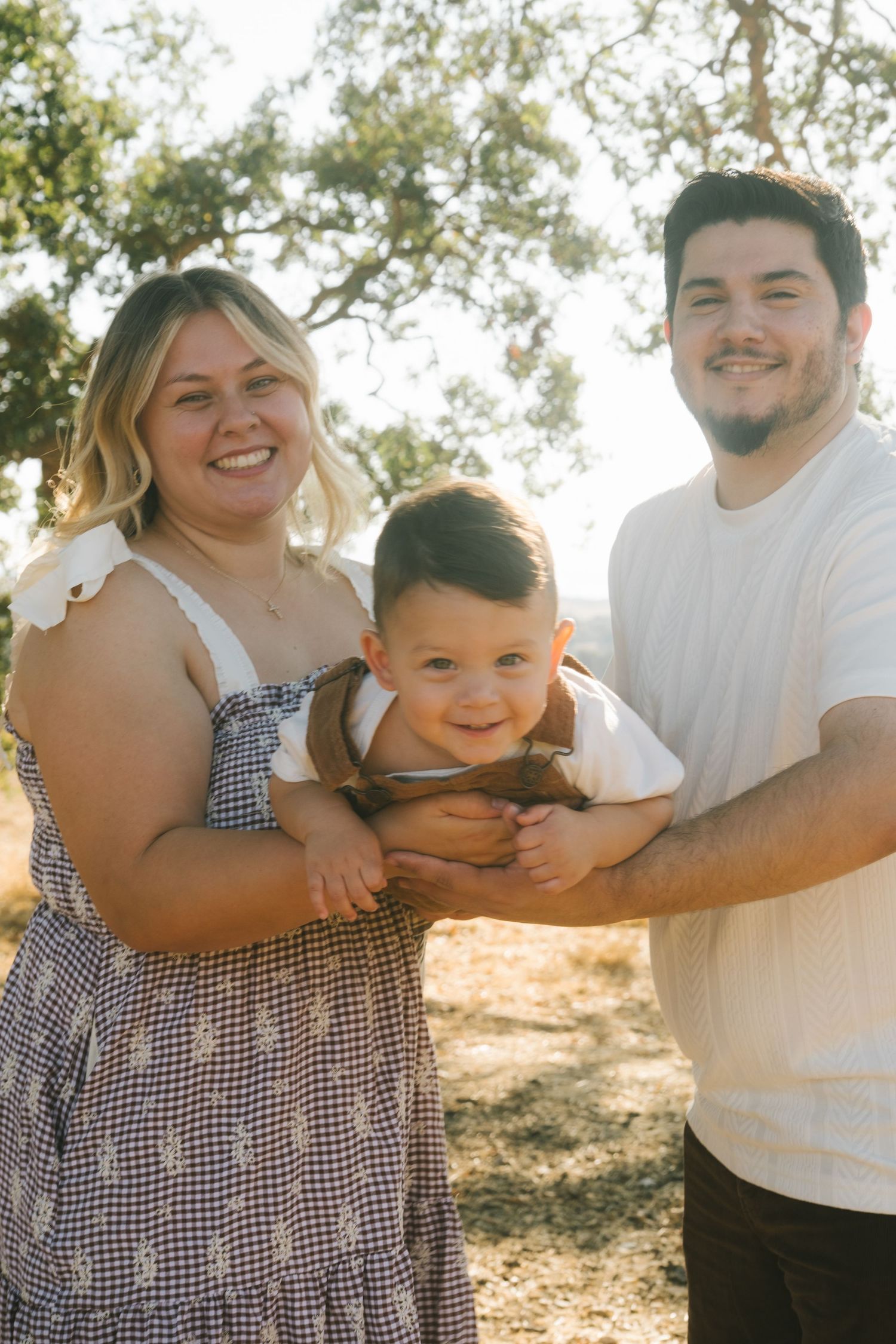 A joyful family moment captured outdoors under trees in warm sunlight.