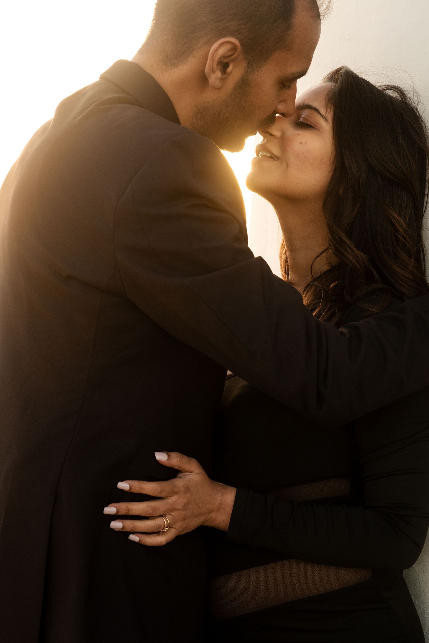A silhouetted couple sharing an intimate moment against a bright backlit background.