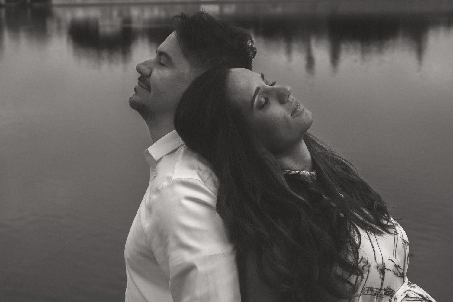 Couple sharing intimate moments by a reflective lake in black and white.
