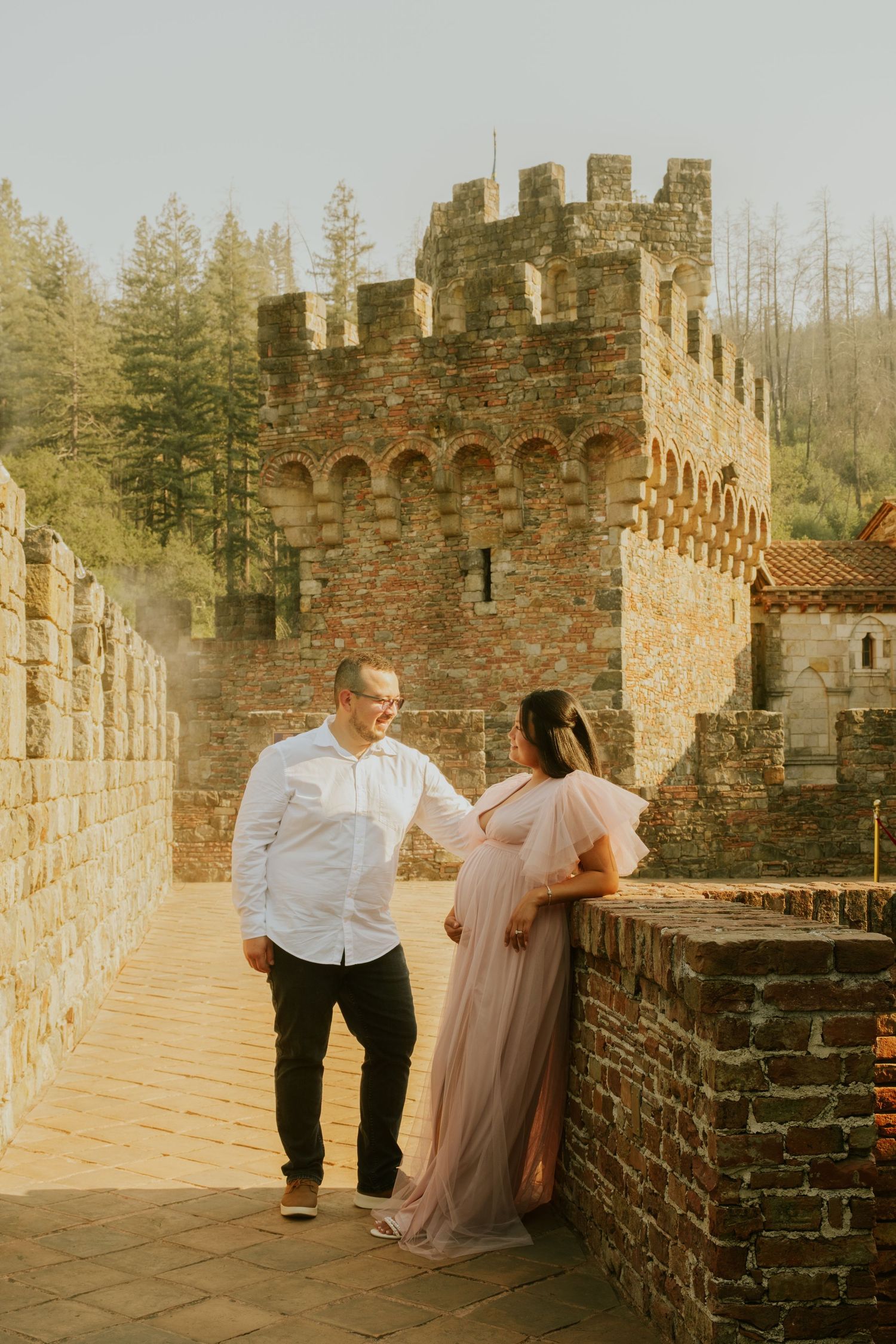 Couple poses together against stone castle walls during golden hour.