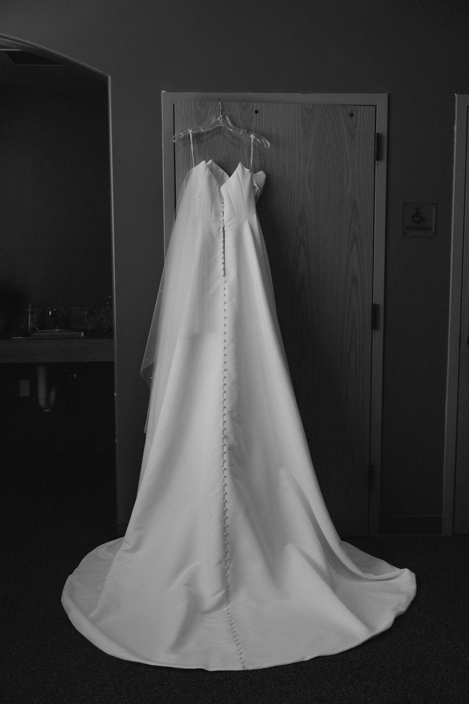 Elegant white wedding dress with a long train hanging on a wooden door in black and white photography.