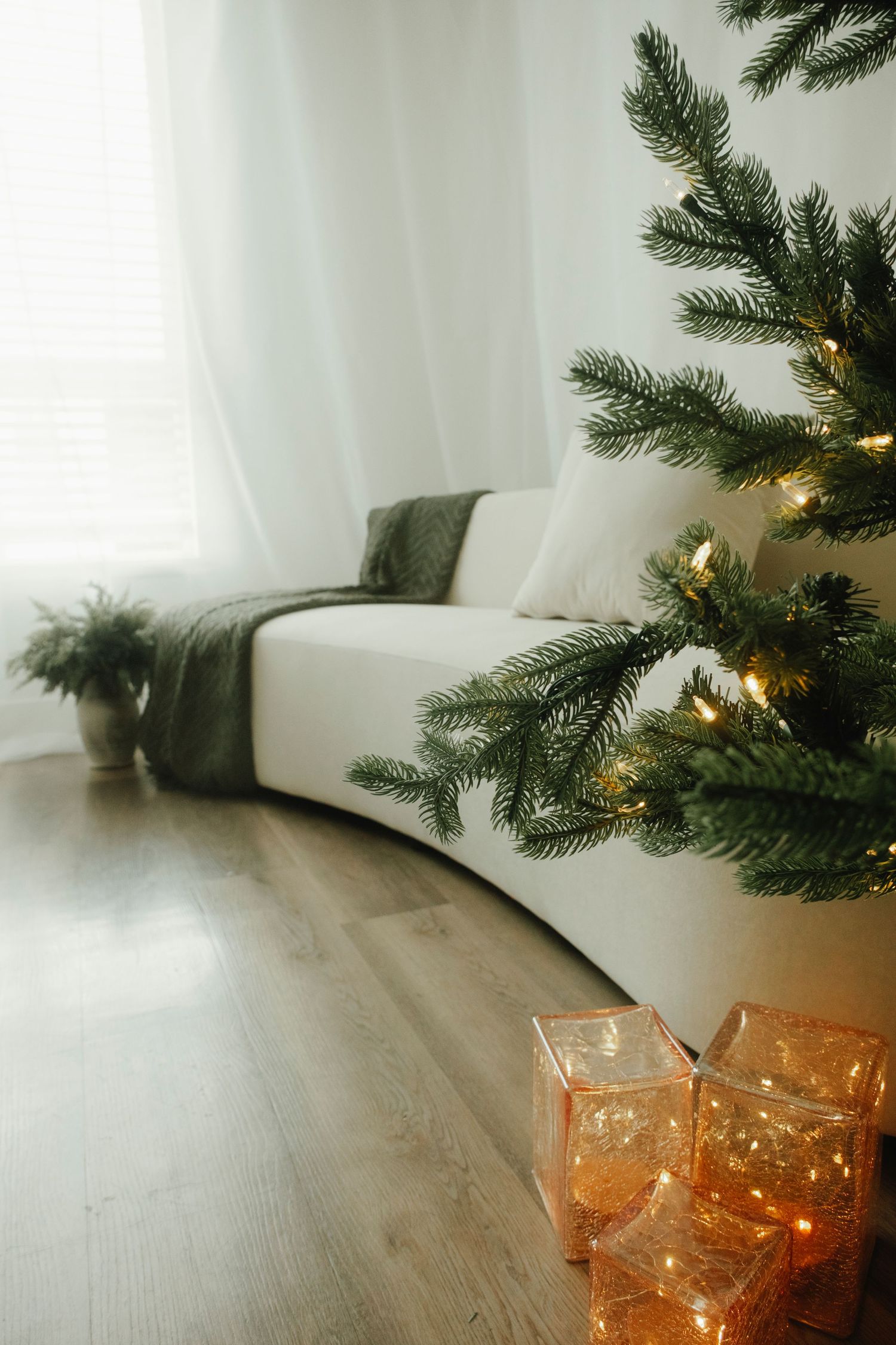 Christmas tree branches with glowing lights and orange glass decorations on a wooden floor.