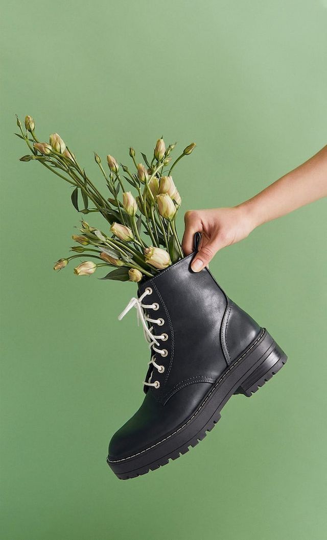 Black combat boots with white flowers arranged inside against a mint green background.