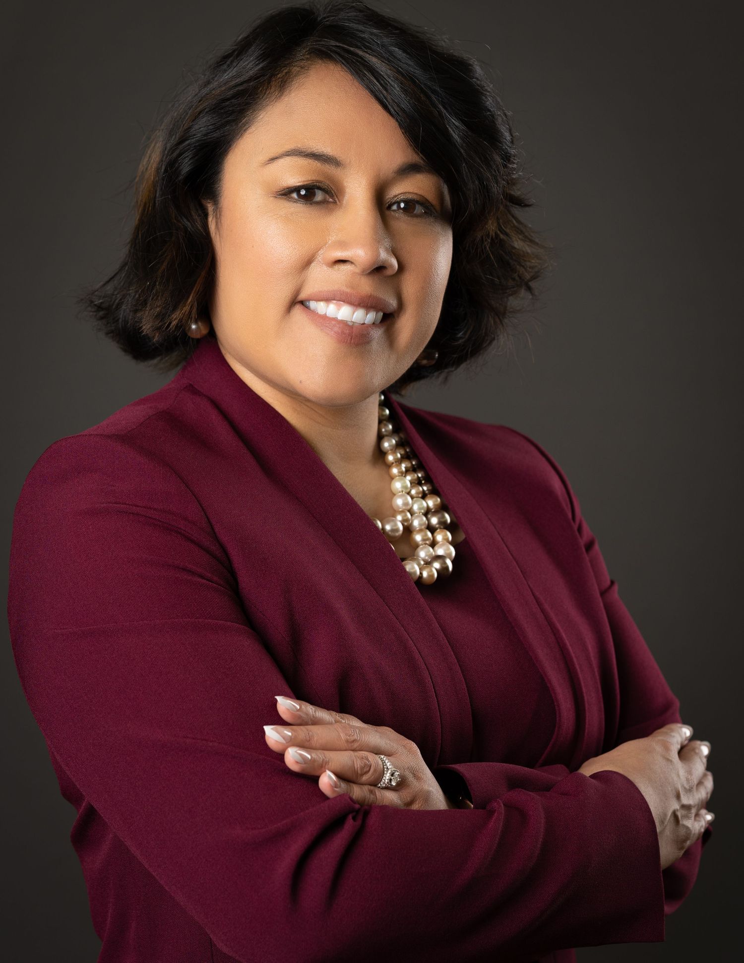 Professional studio portraits show person in burgundy blazer against dark background with gold statement necklace.