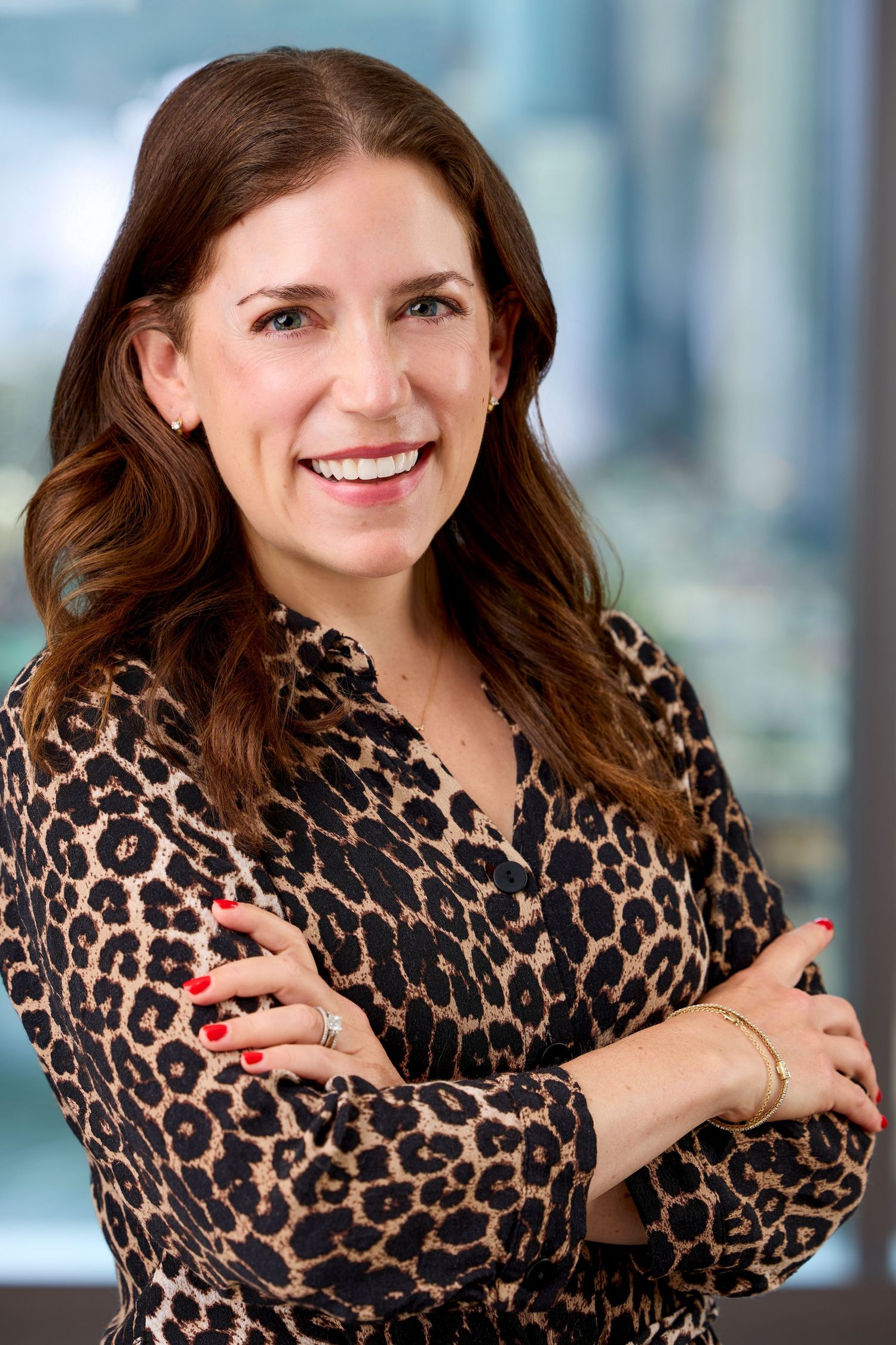 Professional portrait of someone in a leopard print blouse smiling against a blurred office background.