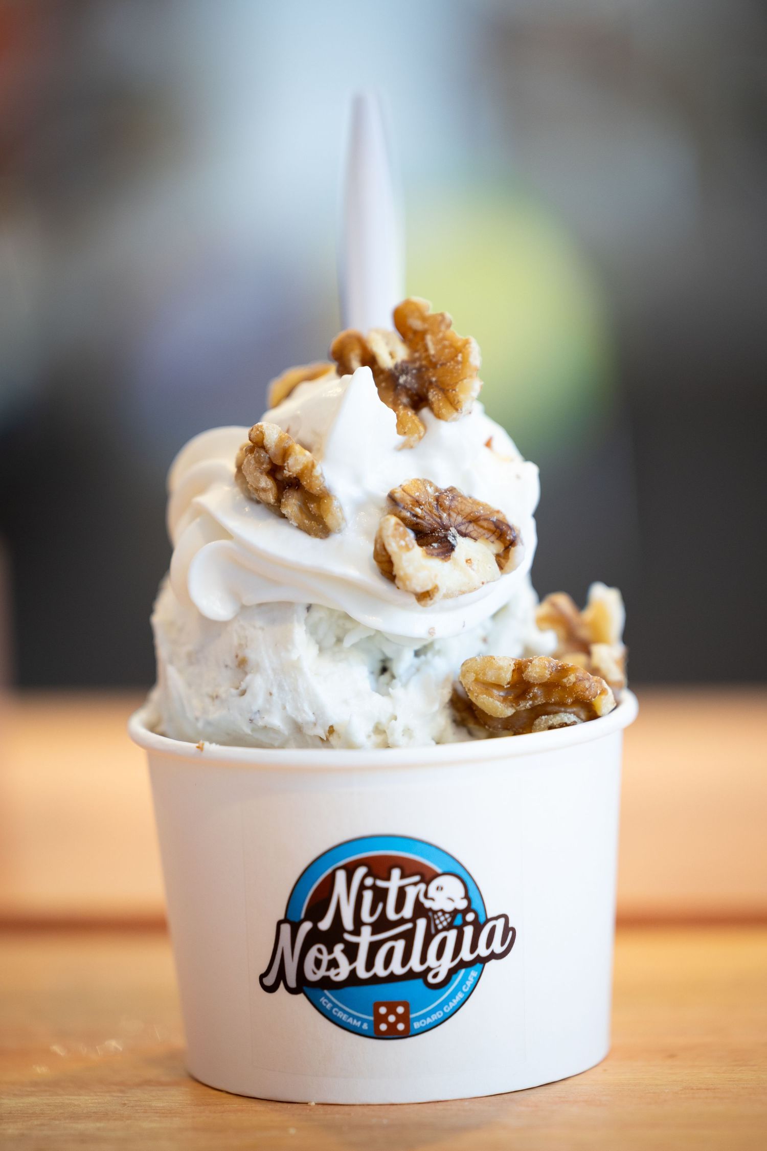 A frozen yogurt dessert topped with walnuts and whipped cream served in a white cup with the Nostalgue logo.
