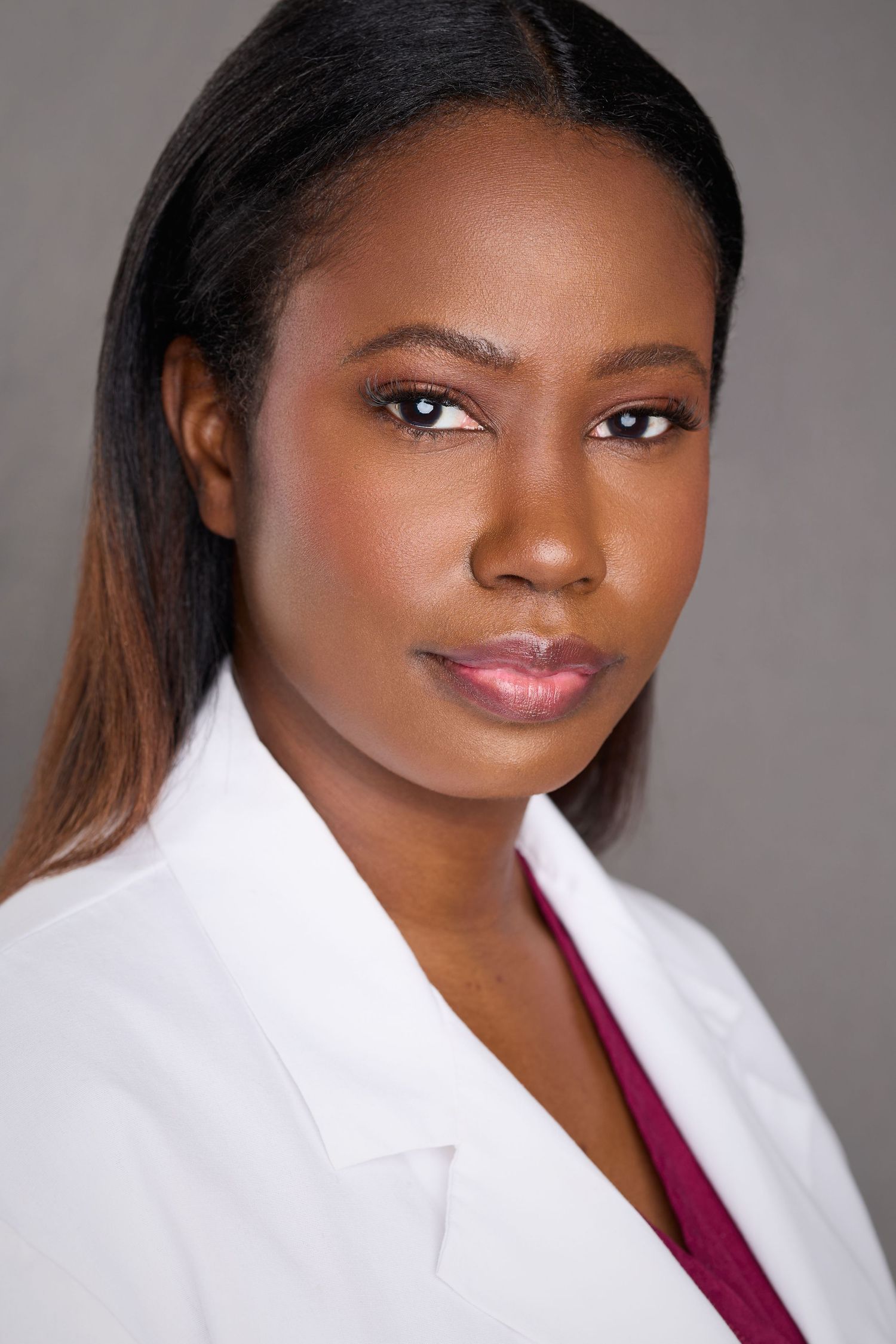 Professional headshot portraits of a healthcare worker in a white coat and burgundy scrubs against a gray background.