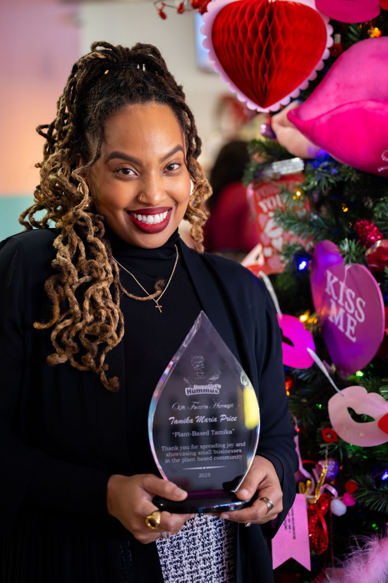 Someone holds a crystal award trophy while standing in front of festive pink and red Valentine's Day decorations.