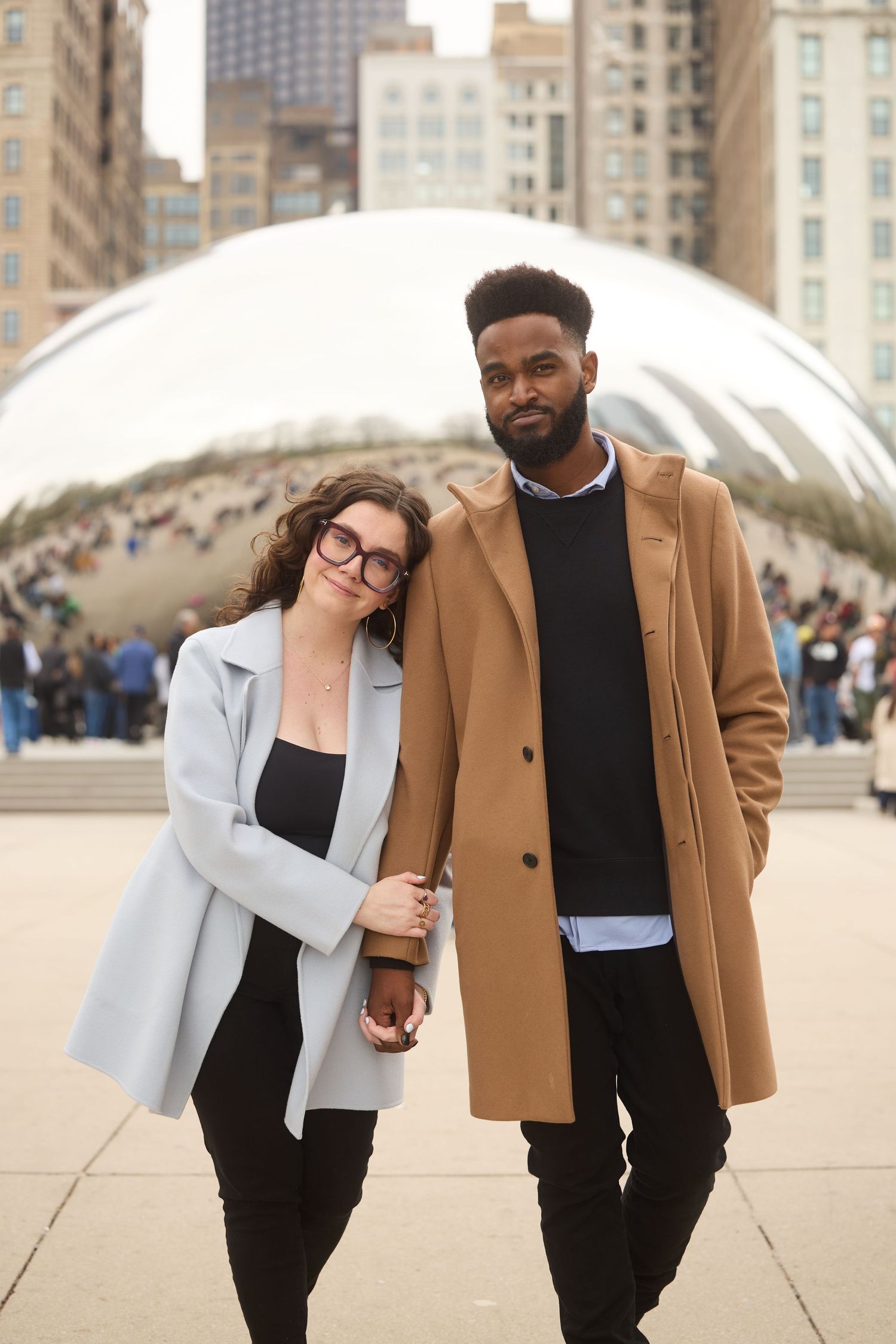 A couple in winter coats holds hands while posing in front of Cloud Gate sculpture at Millennium Park in Chicago.