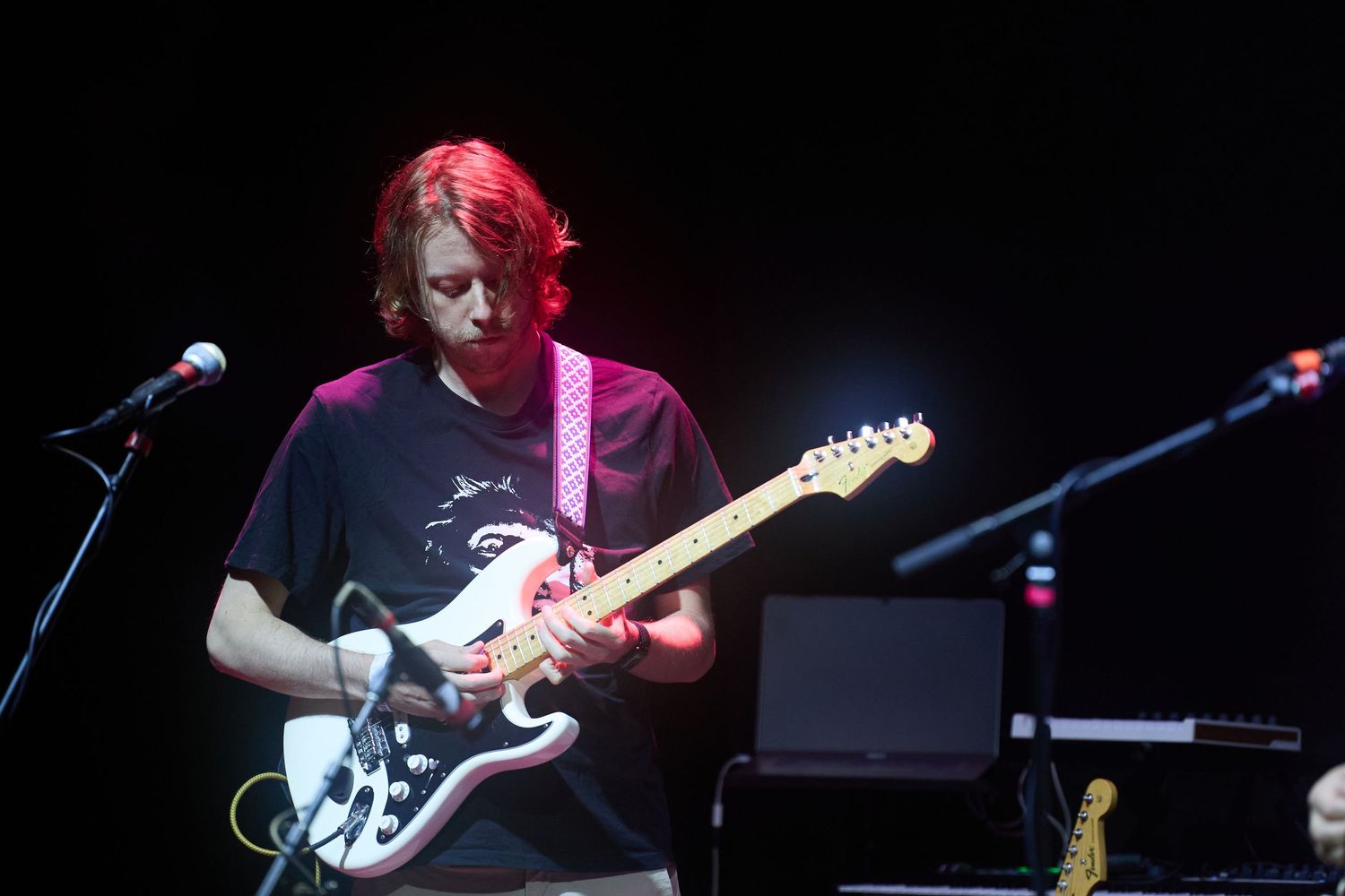 Musician performs on stage with electric guitar under dramatic blue and purple concert lighting.