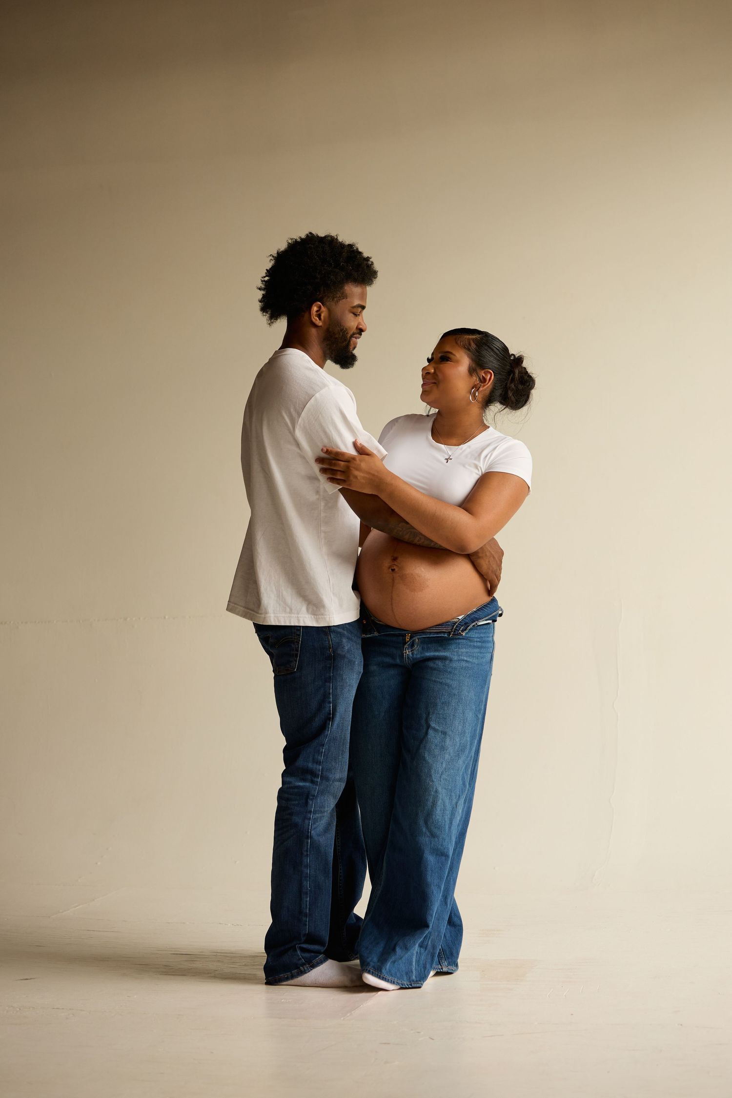 Two people wearing jeans and white shirts embrace in a series of intimate poses against a neutral backdrop.