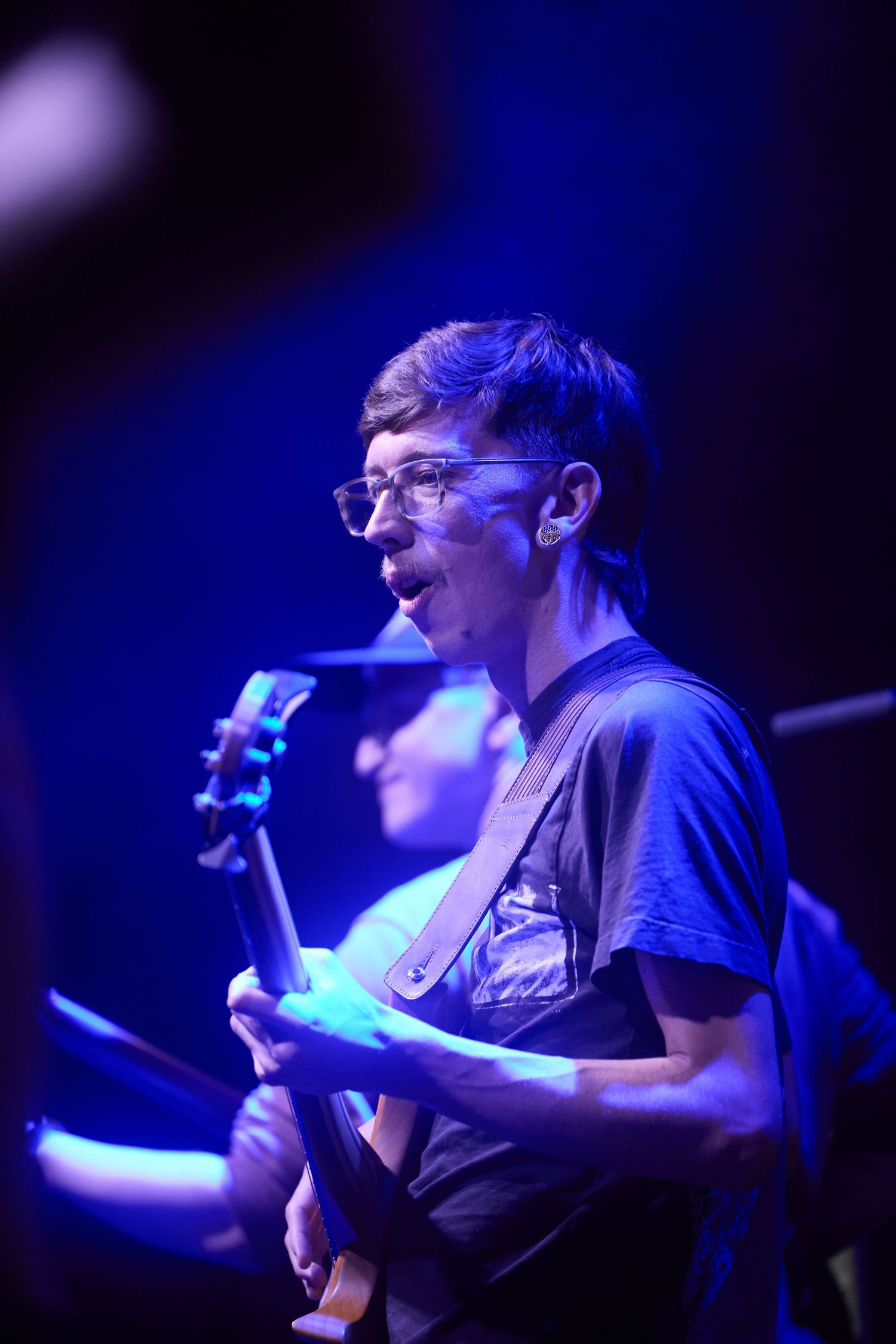 Musician performs on stage in blue lighting while playing guitar during live performance.