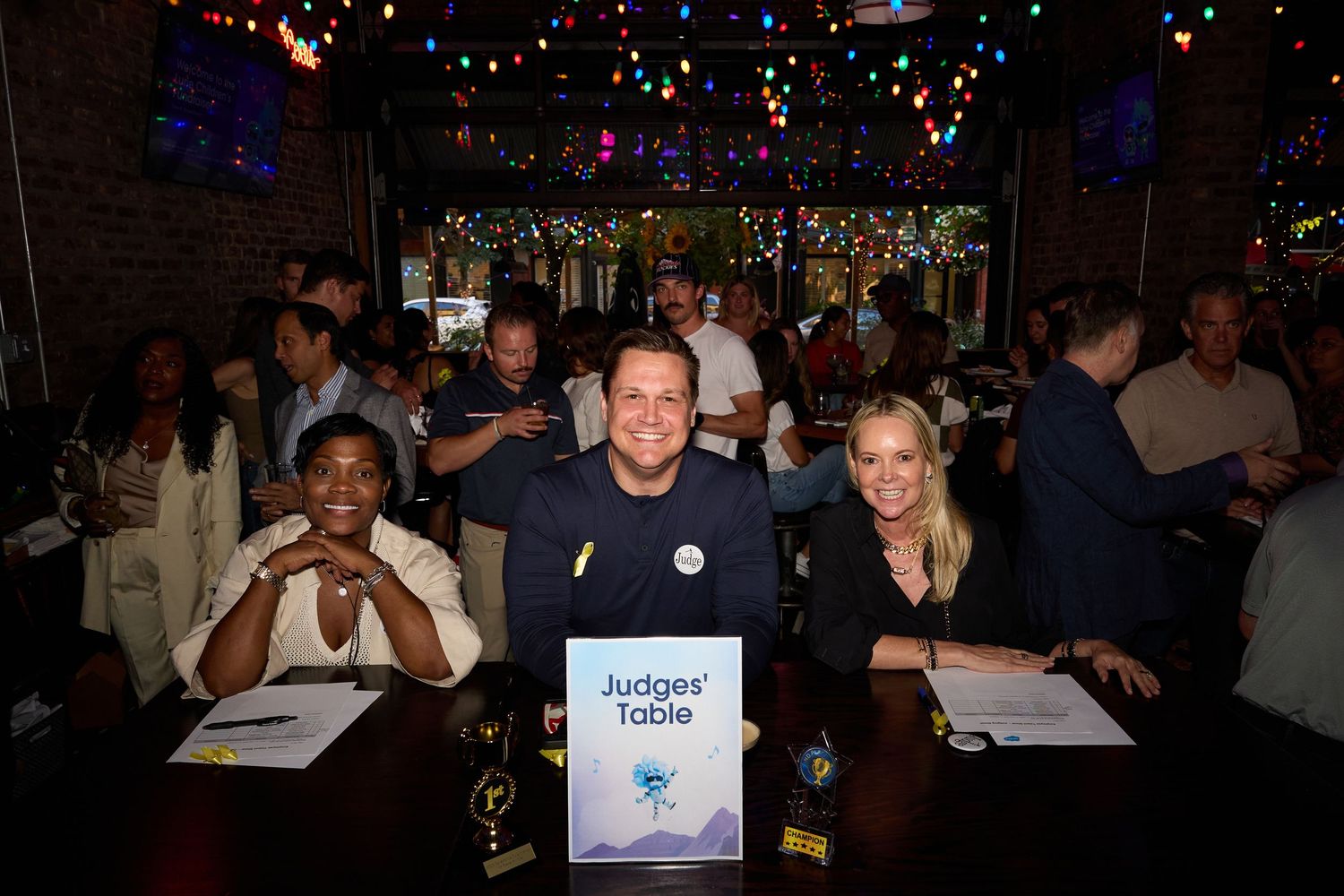 A crowded bar or nightclub interior with colorful string lights and people socializing in a dimly lit atmosphere.