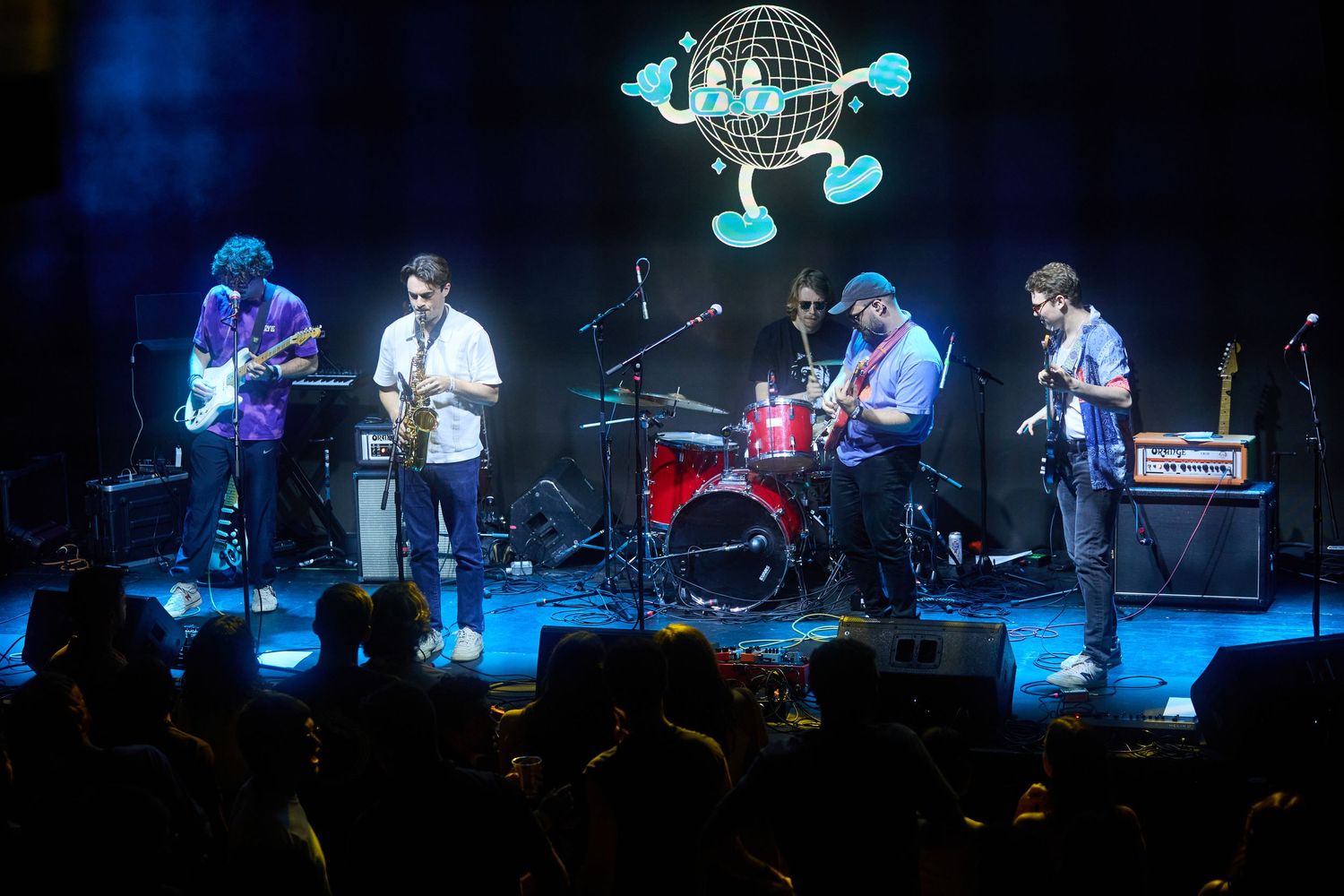 Musicians perform on a dark stage illuminated by blue lighting during a live concert performance.