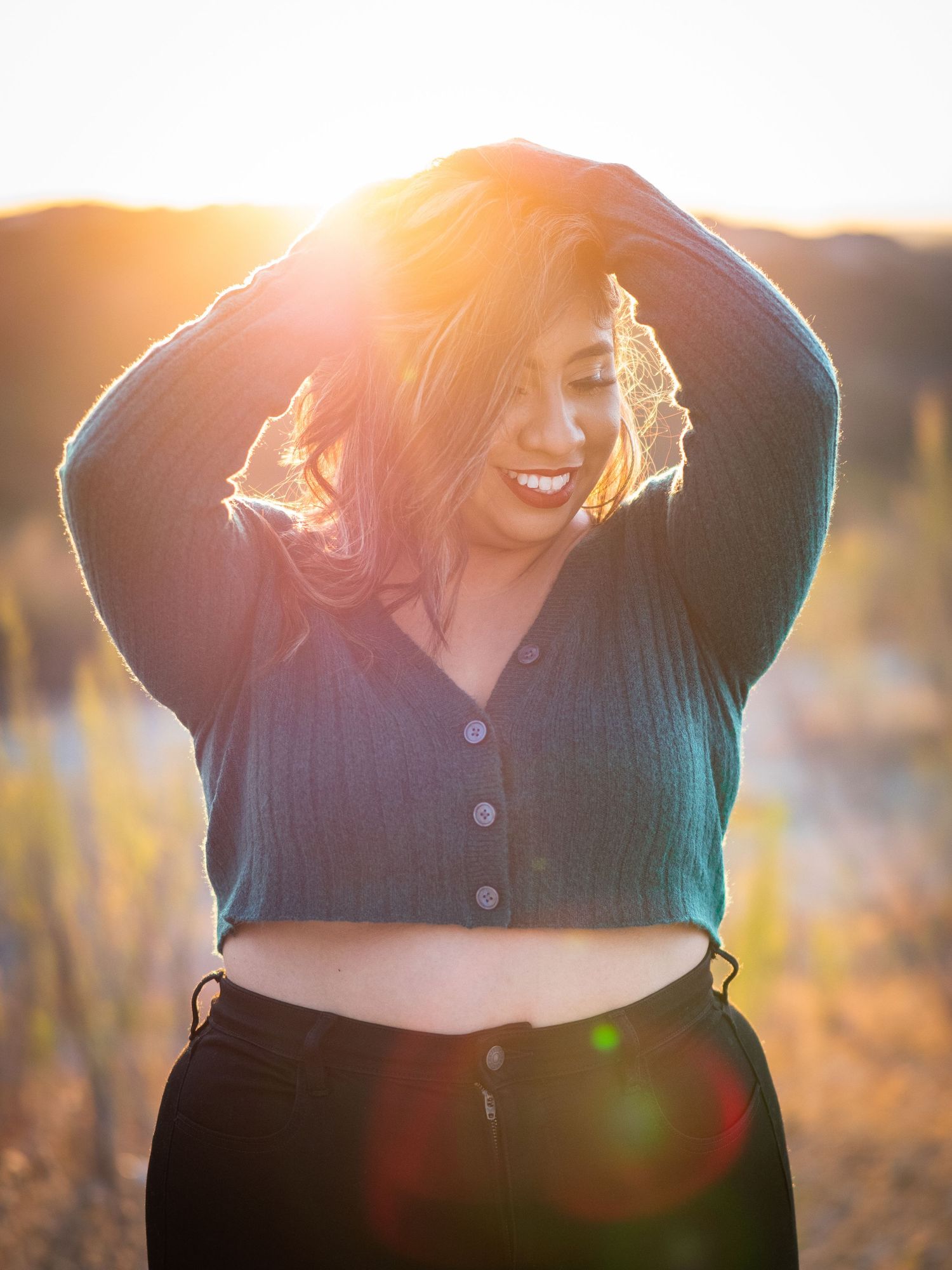 Joyful figure in sunlit field laughs while backlit by golden sunset creating a warm silhouette effect.