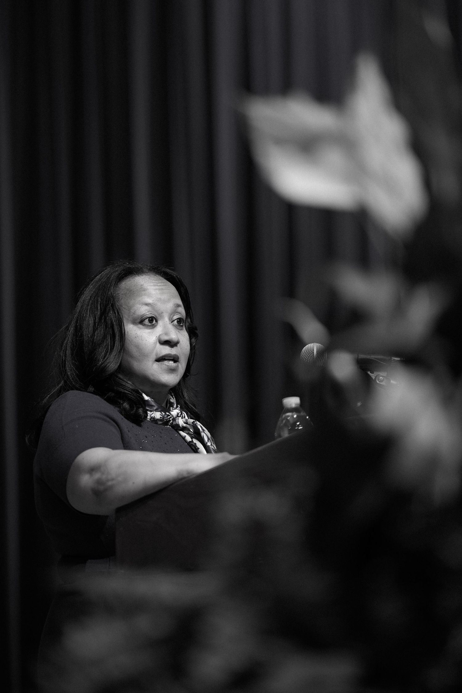 A speaker gestures passionately while giving a presentation in dramatic black and white lighting.