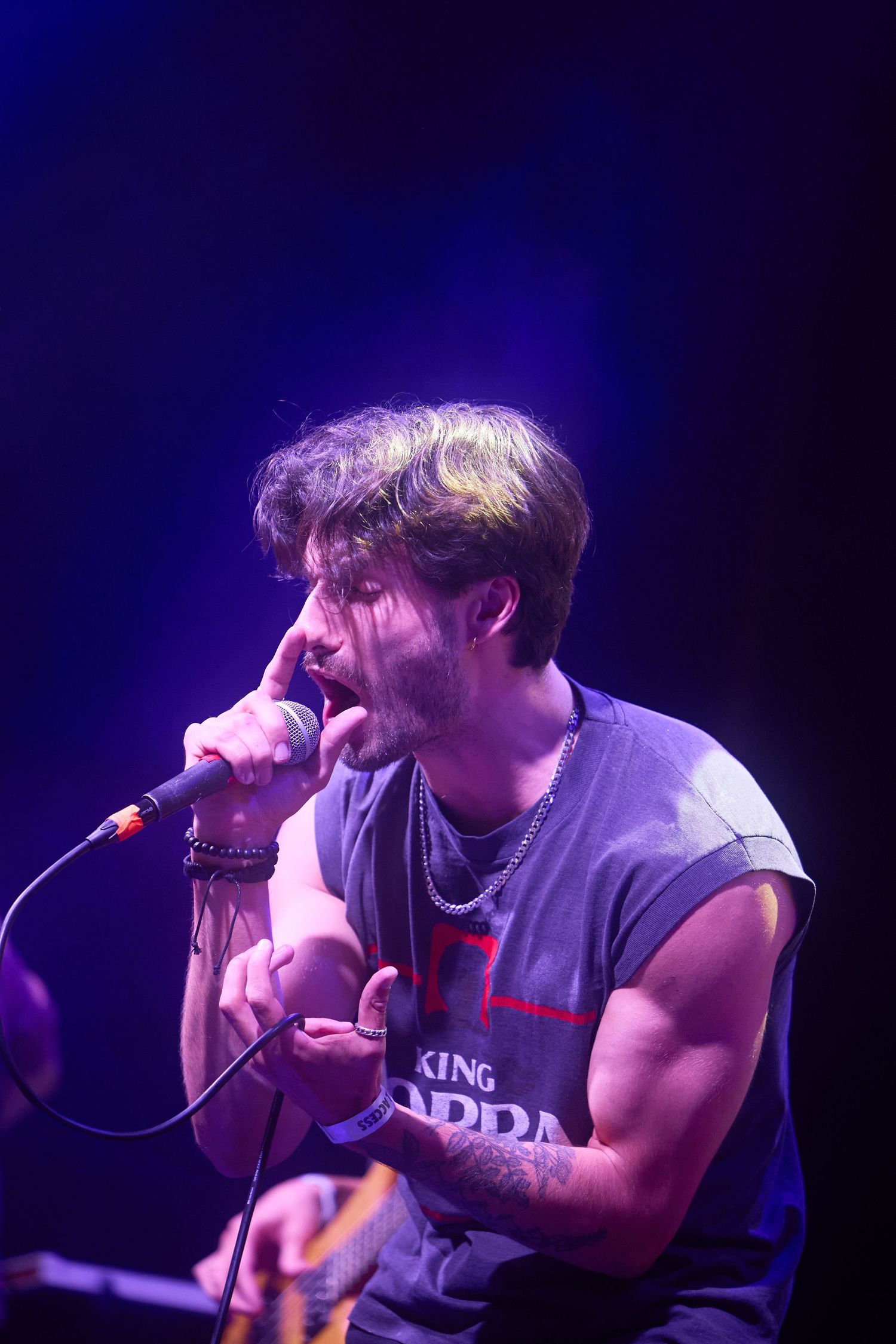 A performer sings passionately into a microphone on a dark stage with dramatic blue lighting.