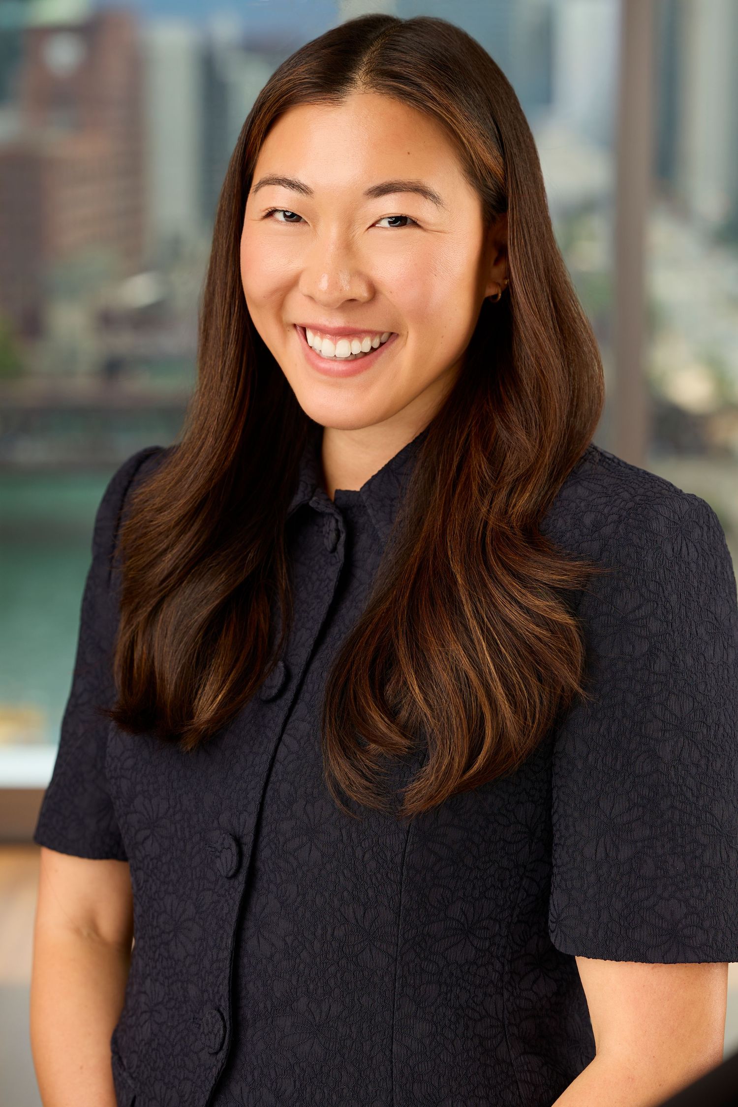 Professional headshot of someone in a black blazer smiling warmly against a blurred office background.