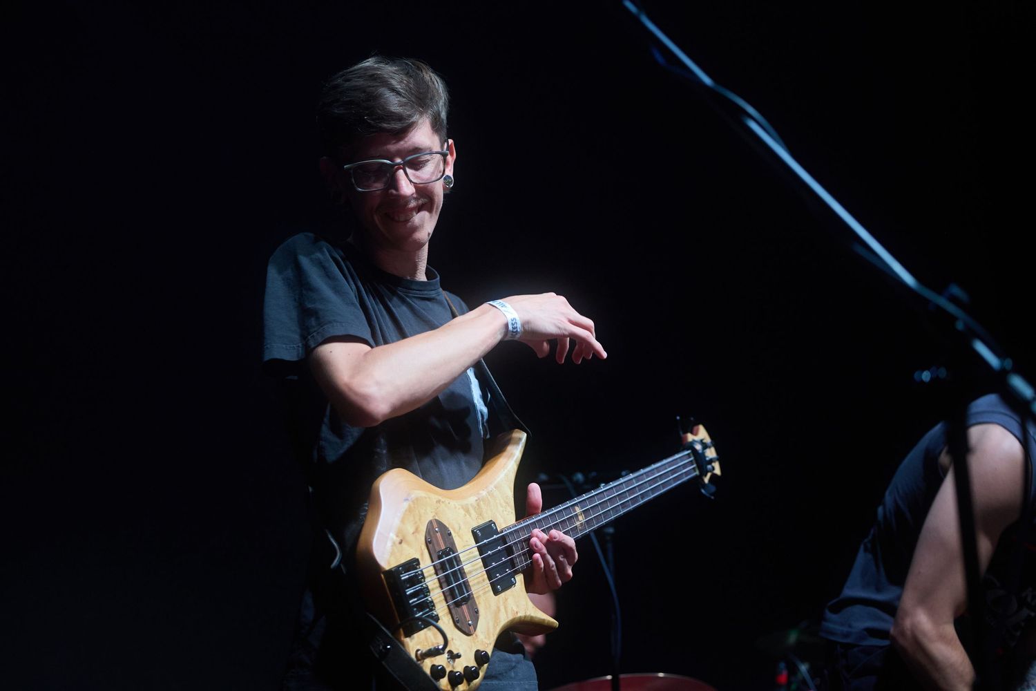 Musician performs on stage with a yellow bass guitar under dramatic blue lighting during a live concert performance.