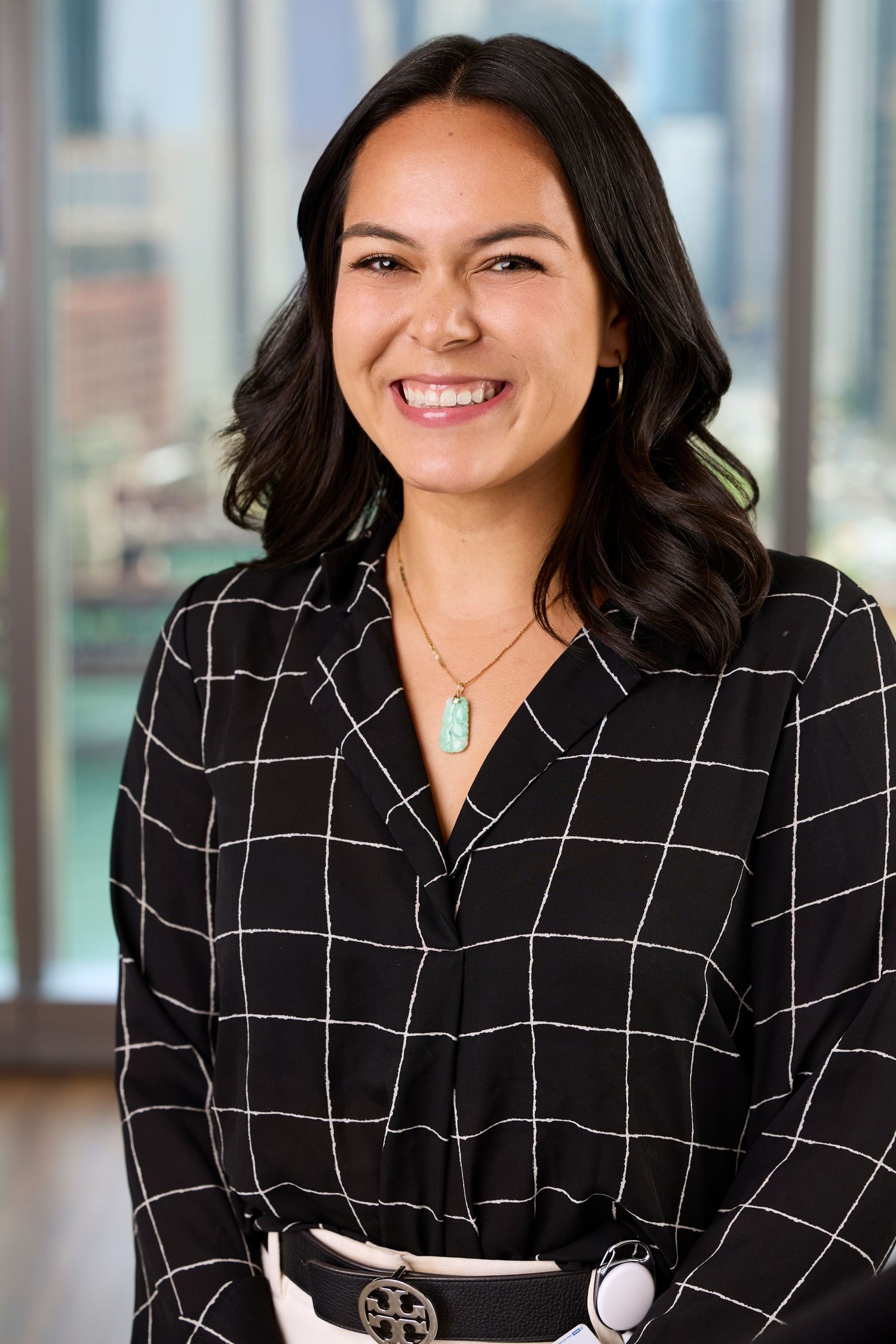 Professional woman in black and white checkered blazer smiling warmly in modern office setting.