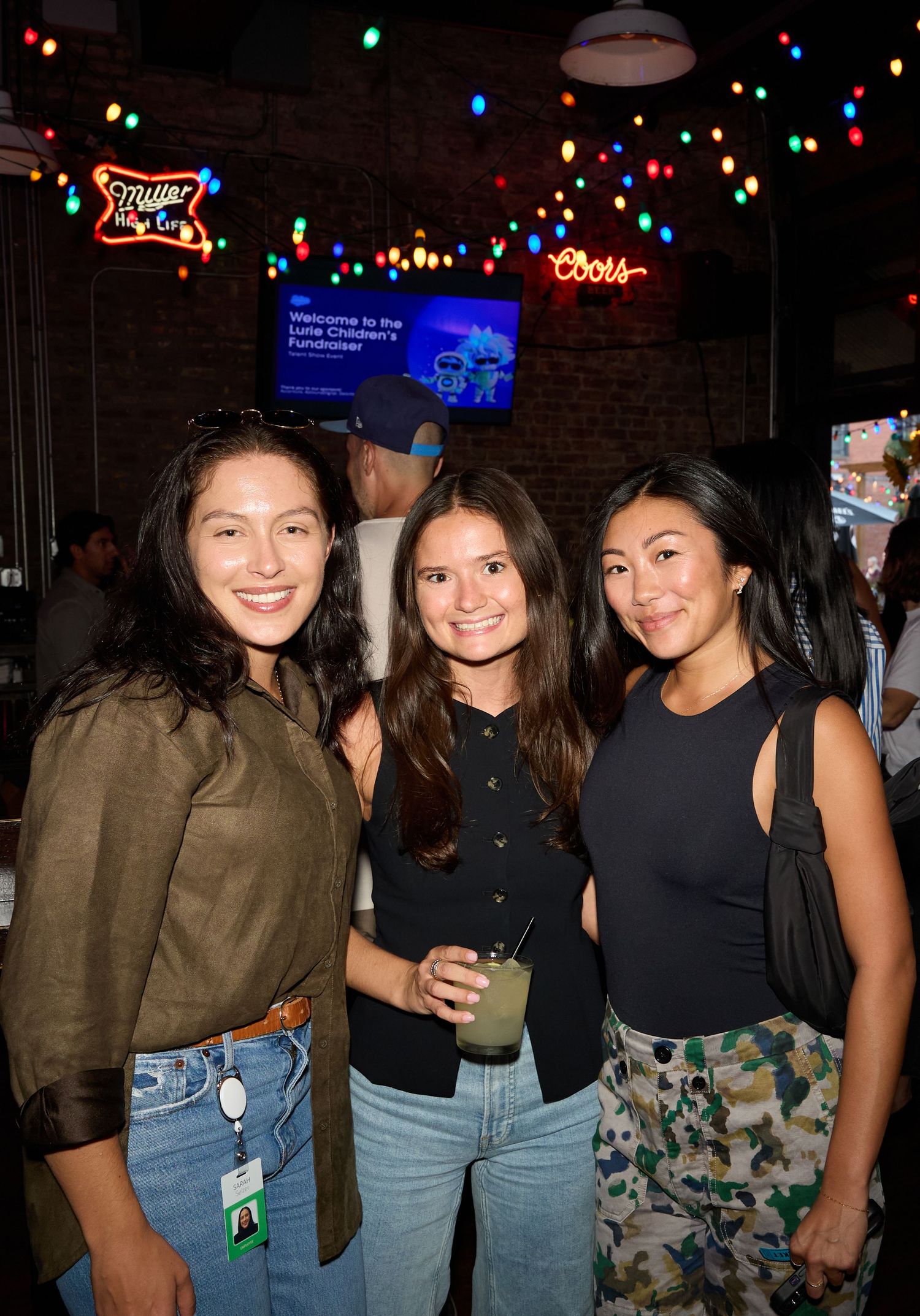 Group of friends in coordinated outfits with jeans and dark tops enjoying a night out at a bar with festive lights.