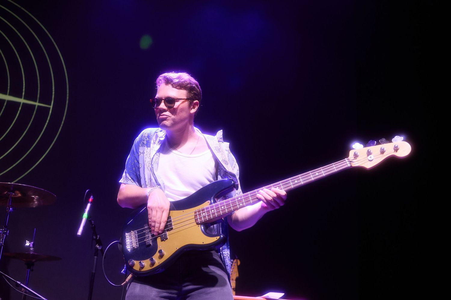 Bass guitarist performs on stage with a yellow bass guitar under blue concert lighting.