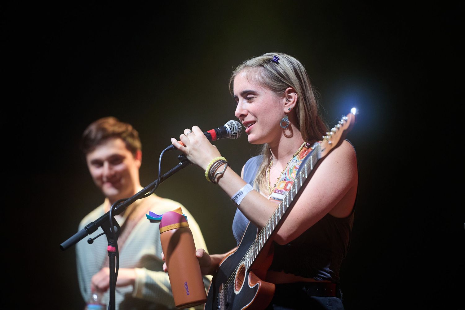 A performer sings passionately into a microphone on a dimly lit stage during a live concert performance.
