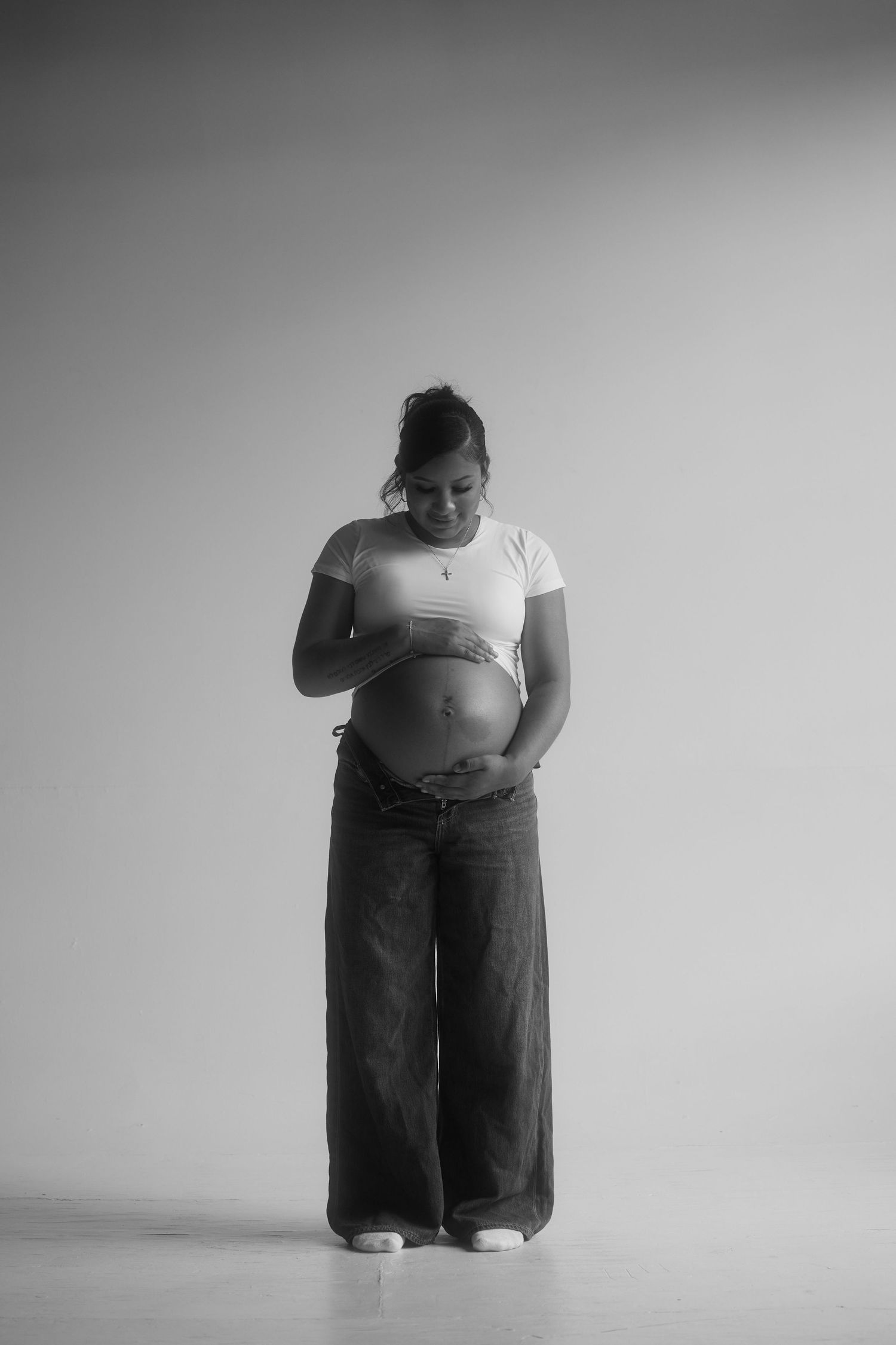 A black and white photo series shows a 8 month pregnant woman in dark pants against a white background demonstrating different poses.
