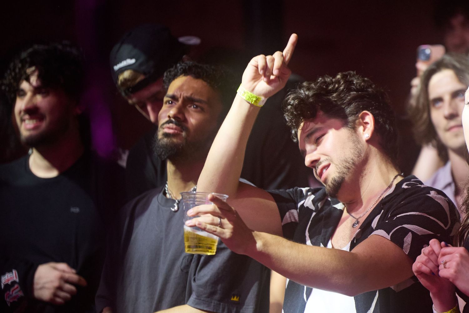 A crowded concert venue with people enjoying drinks and dancing to music in a dark nightclub atmosphere.