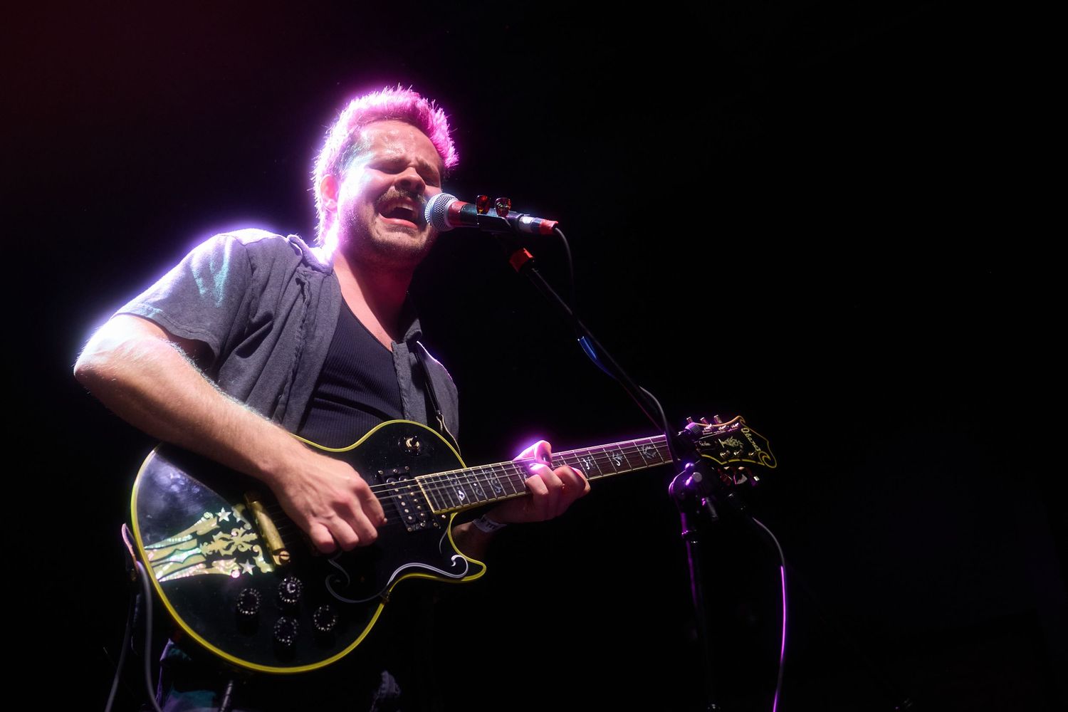 A musician performs on stage with an acoustic guitar under dramatic purple and blue stage lighting.