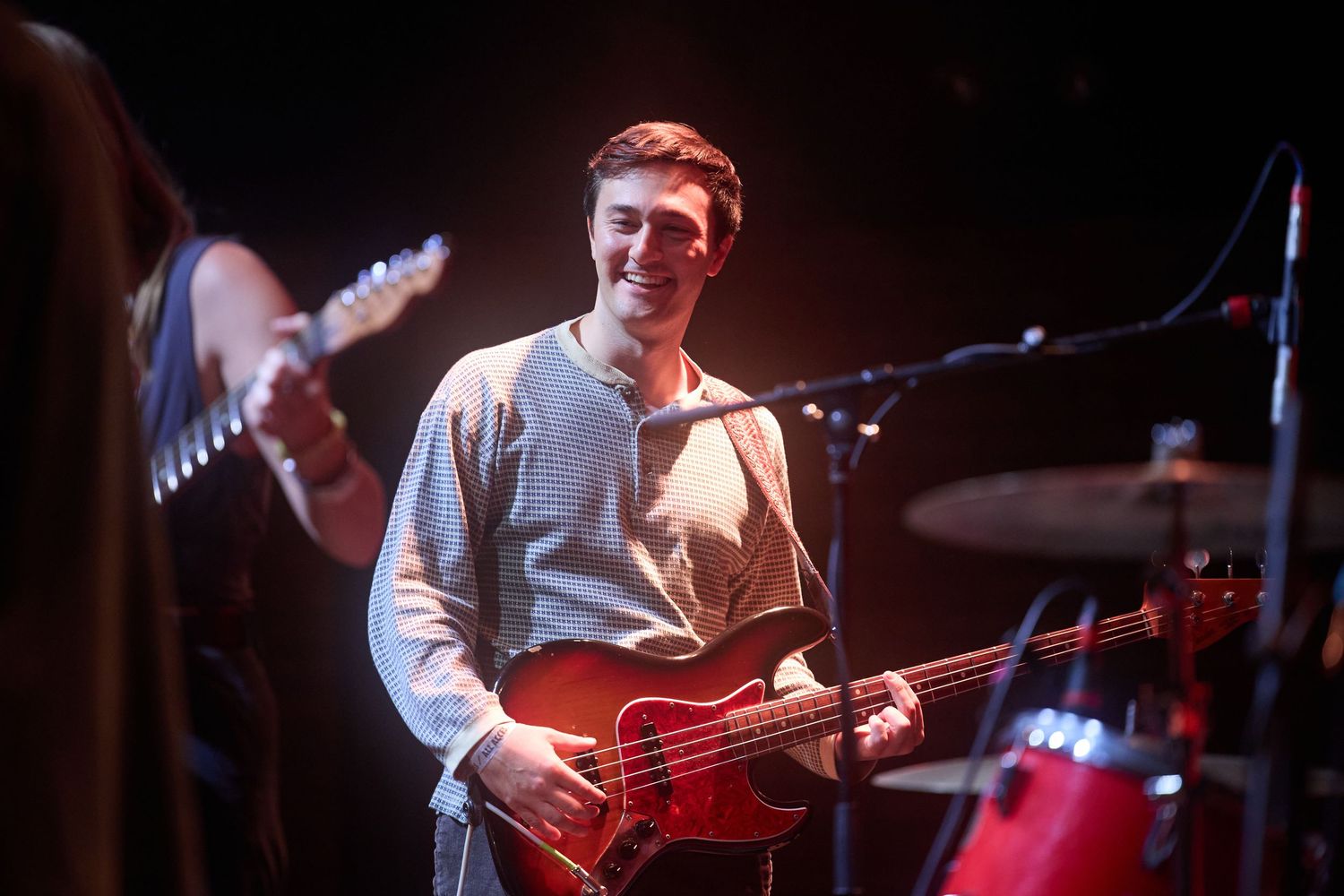 Musicians perform on stage with guitars and drums during a live concert in dark lighting.