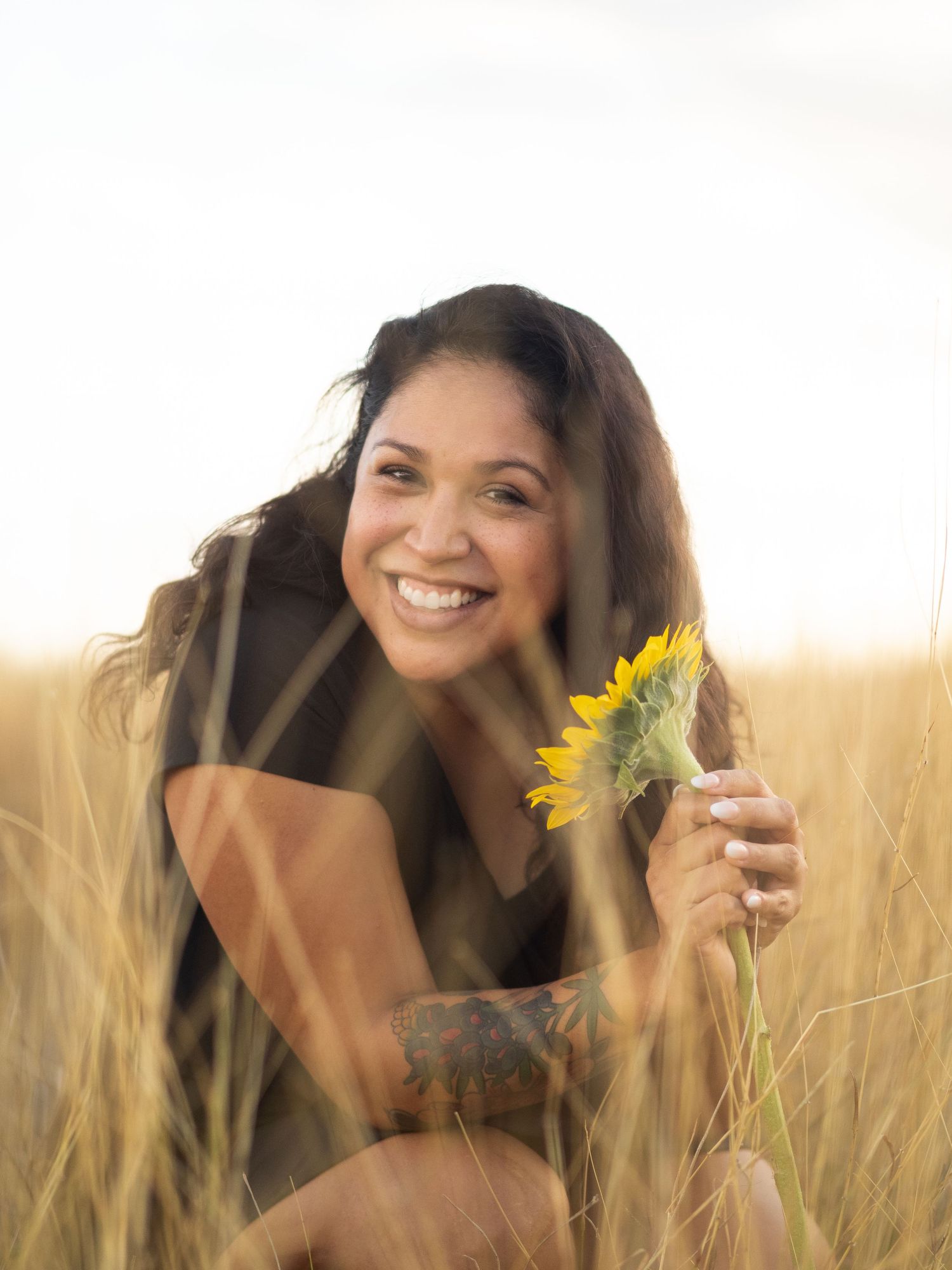 A person poses joyfully in a golden wheat field with sunflowers during sunset creating a warm and dreamy atmosphere.