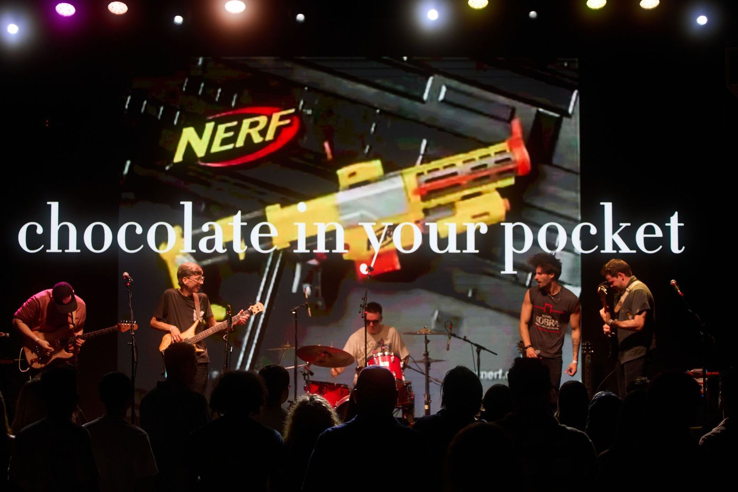 A band performs on stage under colorful lights with a Nerf logo and 'chocolate in your pocket' text overlay.