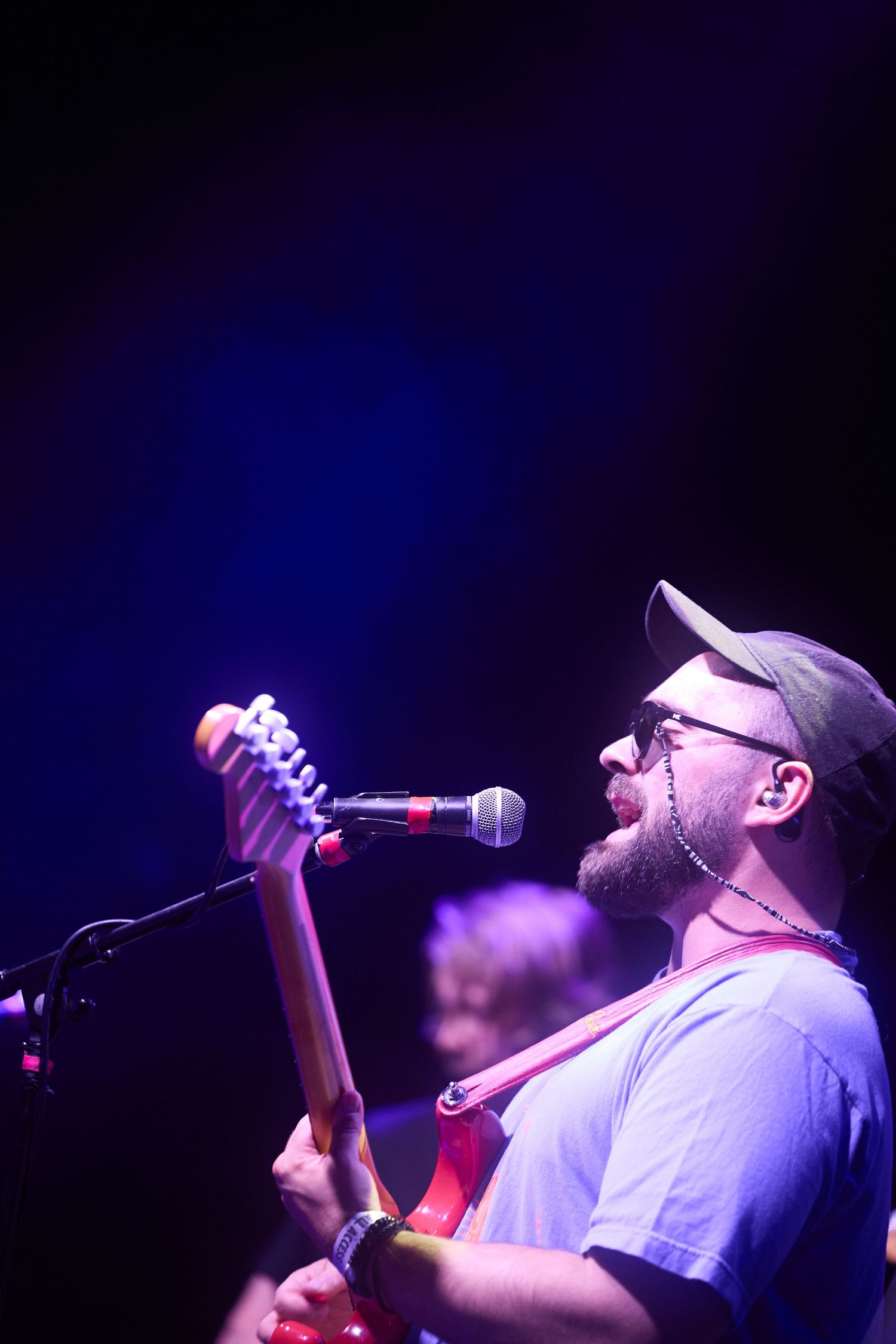 Performer singing passionately into microphone on dark stage with blue lighting during live concert performance.
