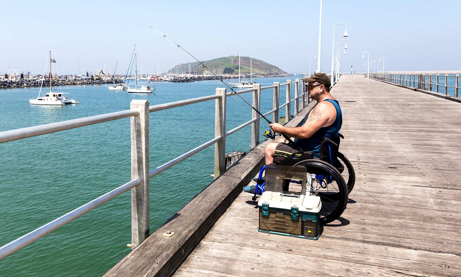 Man in wheelchair fishing from Coffs Harbour Jetty, capturing resilience, independence, quiet contemplation. Photo by Raymond Mather.