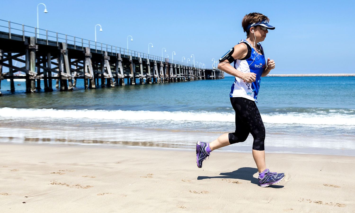 Colour photograph of runner on beach near Coffs Harbour Jetty, capturing energy, movement, and wellness. Photo by Raymond Mather.