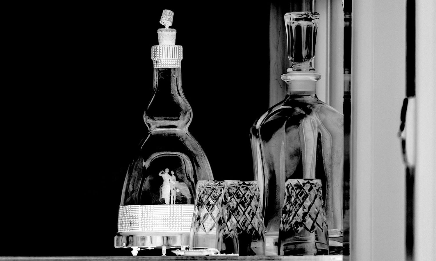 Black and white photograph of liquor bottles silhouetted against a window with dramatic lighting and shadows.